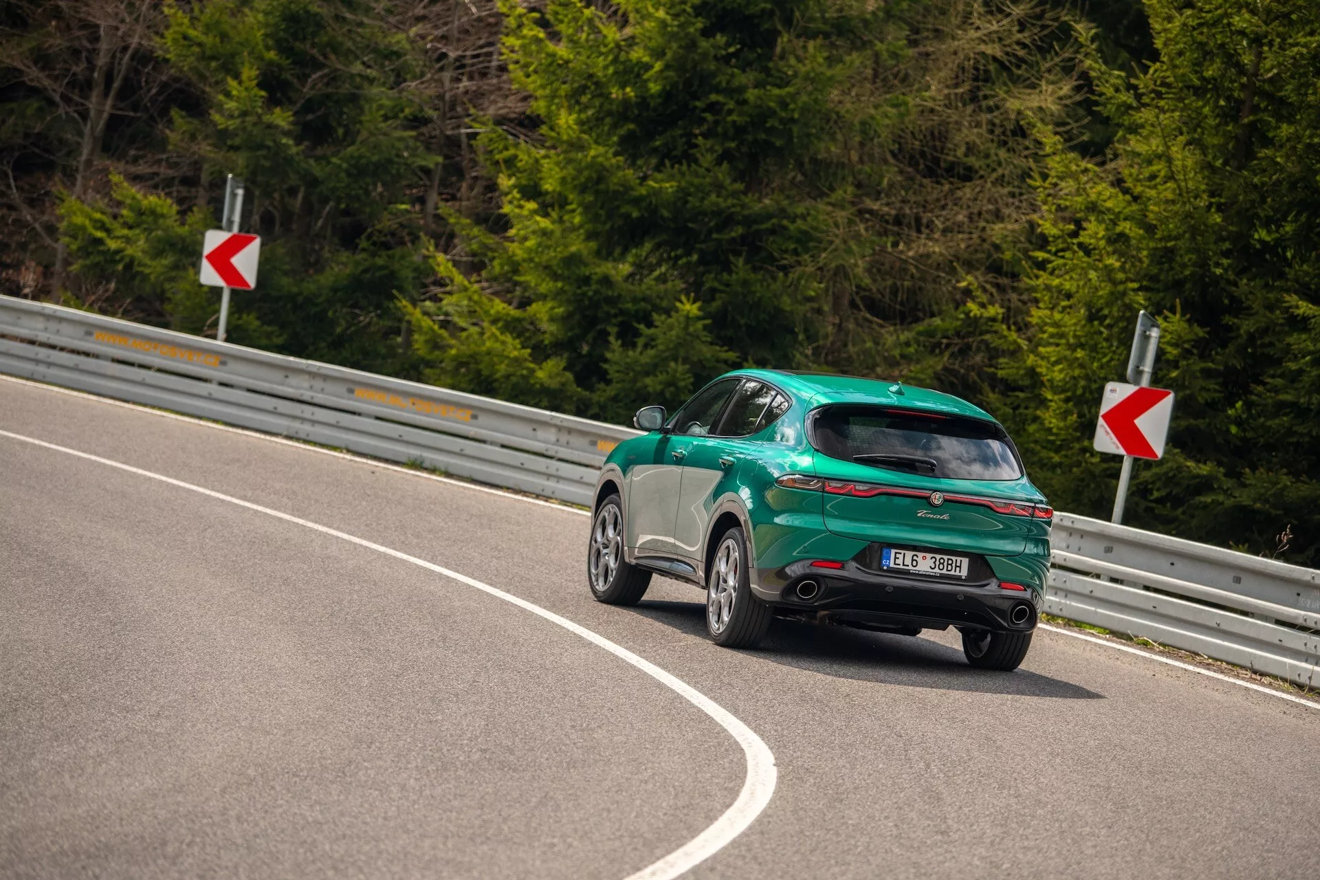 Alfa Romeo Tonale 2022 posnet iz zadnjega kota tri četrtine na ovinkasti cesti, ki poudarja športno obliko hatchback, sijajni zaključek in aerodinamične značilnosti, vključno z zadnjim spojlerjem, platišči iz zlitine in LED zadnjimi lučmi.