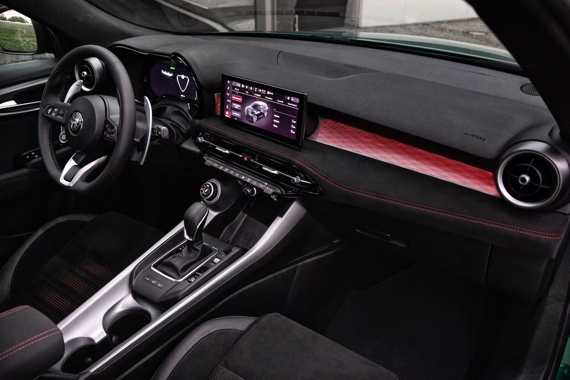 Notranjost Alfa Romeo Tonale 2022 z moderno armaturno ploščo, digitalnim infotainment središčem, poudarki iz ogljikovih vlaken in sedeži z rdečimi šivi, pogled s strani sovoznika