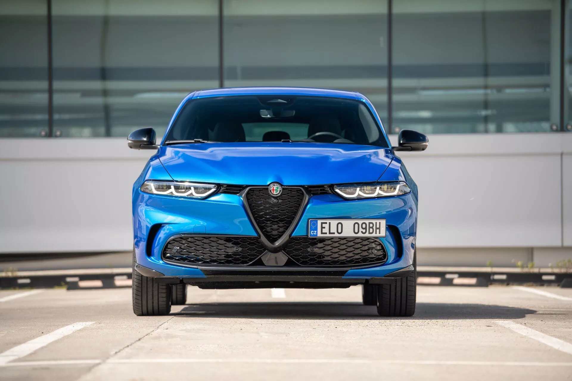 Modri Alfa Romeo Tonale 2022, sprednji pogled na parkirišču prikazuje rešetko z emblemo, LED žaromete in aerodinamične oblikovne značilnosti