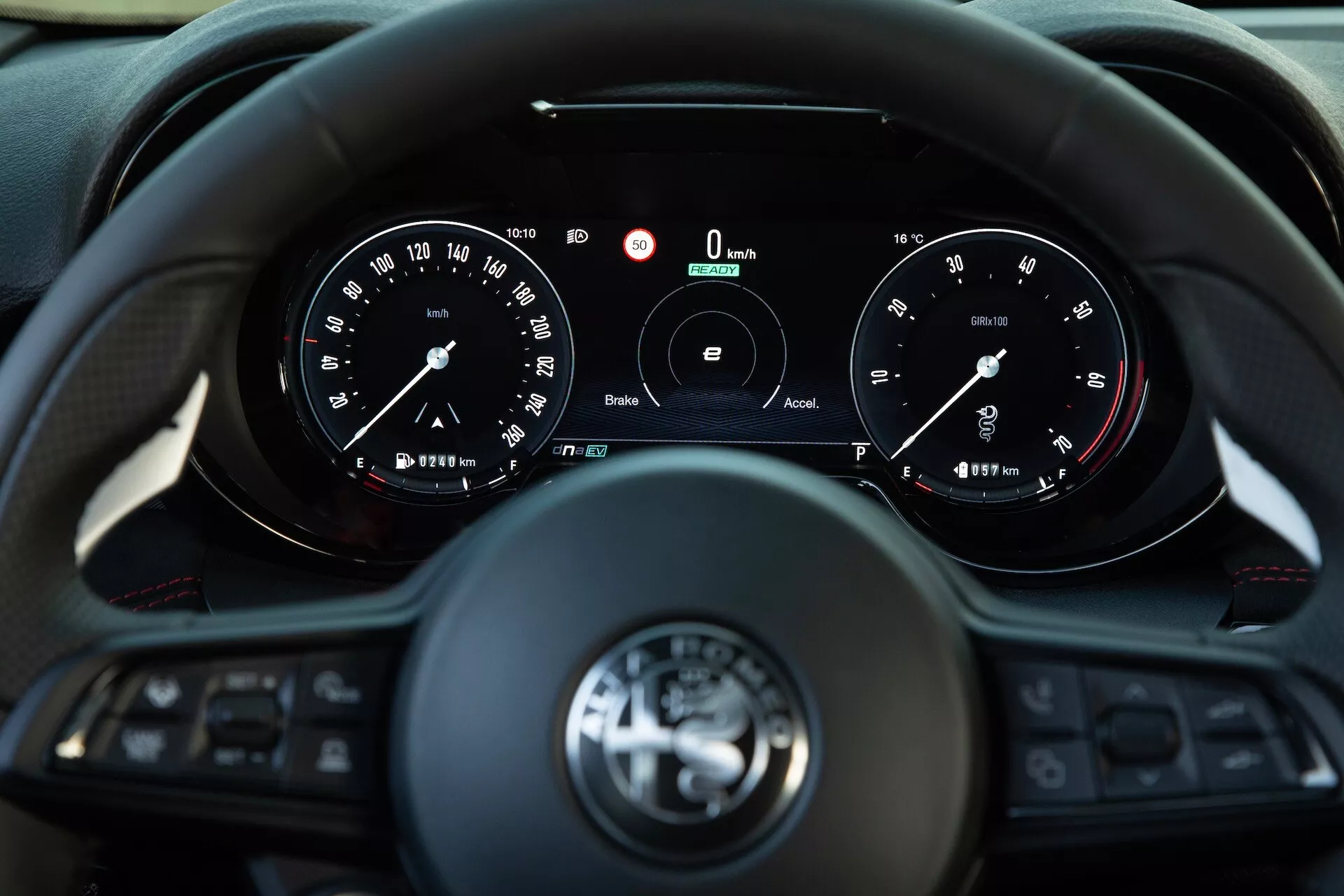 Notranjost Alfa Romeo Tonale 2022 prikazuje pogled voznika na večnamensko volansko obročje s tremi kraki in instrumentno ploščo z analognimi merilniki in centralnim digitalnim zaslonom, ki kaže ničelno hitrost in vrtljaje, s tehnologijami za povezljivost in pomoč vozniku