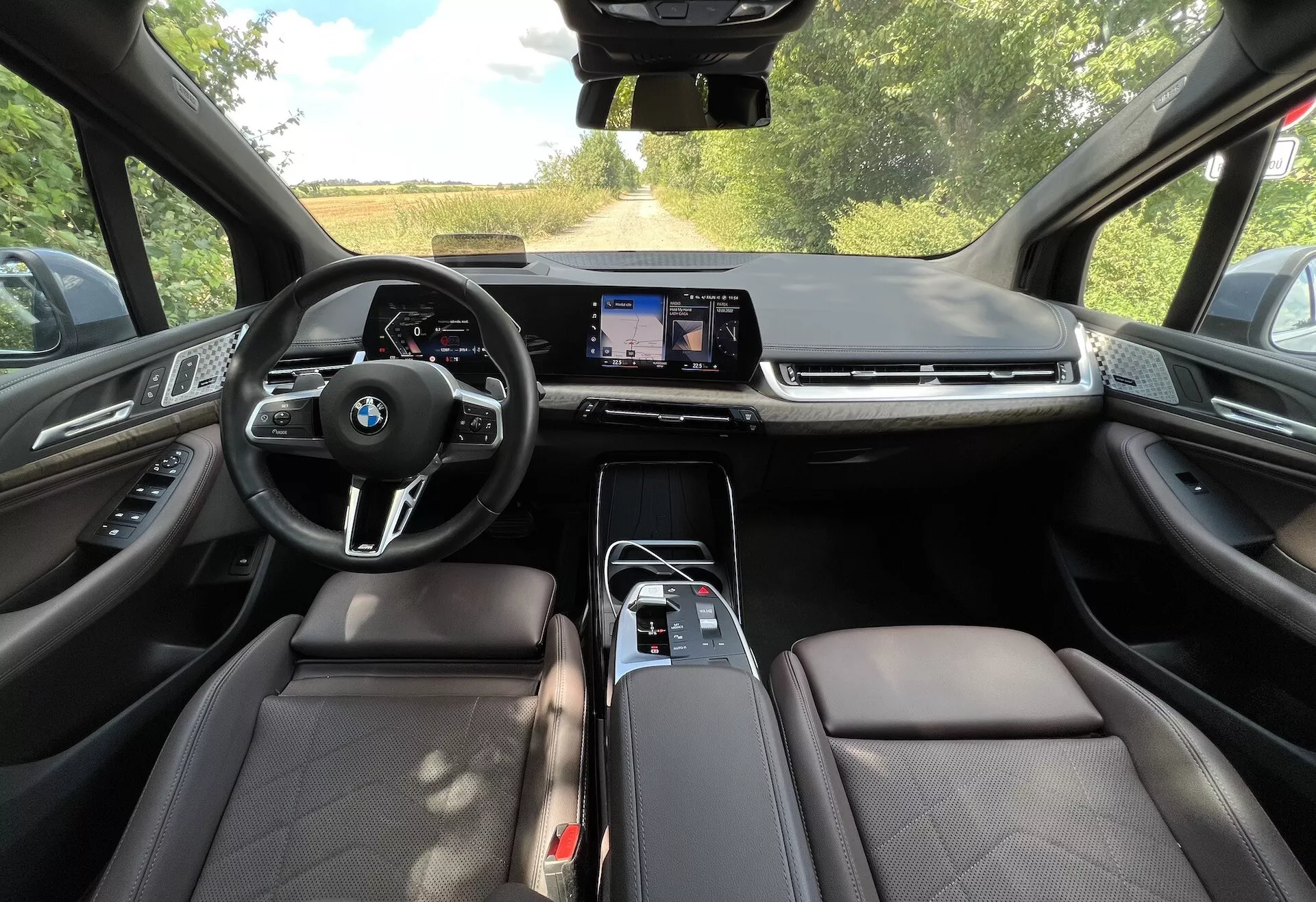 Notranji pogled BMW serije 2 Active Gran Tourer 2022 z večfunkcijskim volanom z logotipom BMW, velikim zaslonom na dotik za informacijsko-razvedrilni sistem, sedeži, oblečenimi v usnje, in naprednimi tehnološkimi funkcijami iz perspektive voznikovega sedeža.