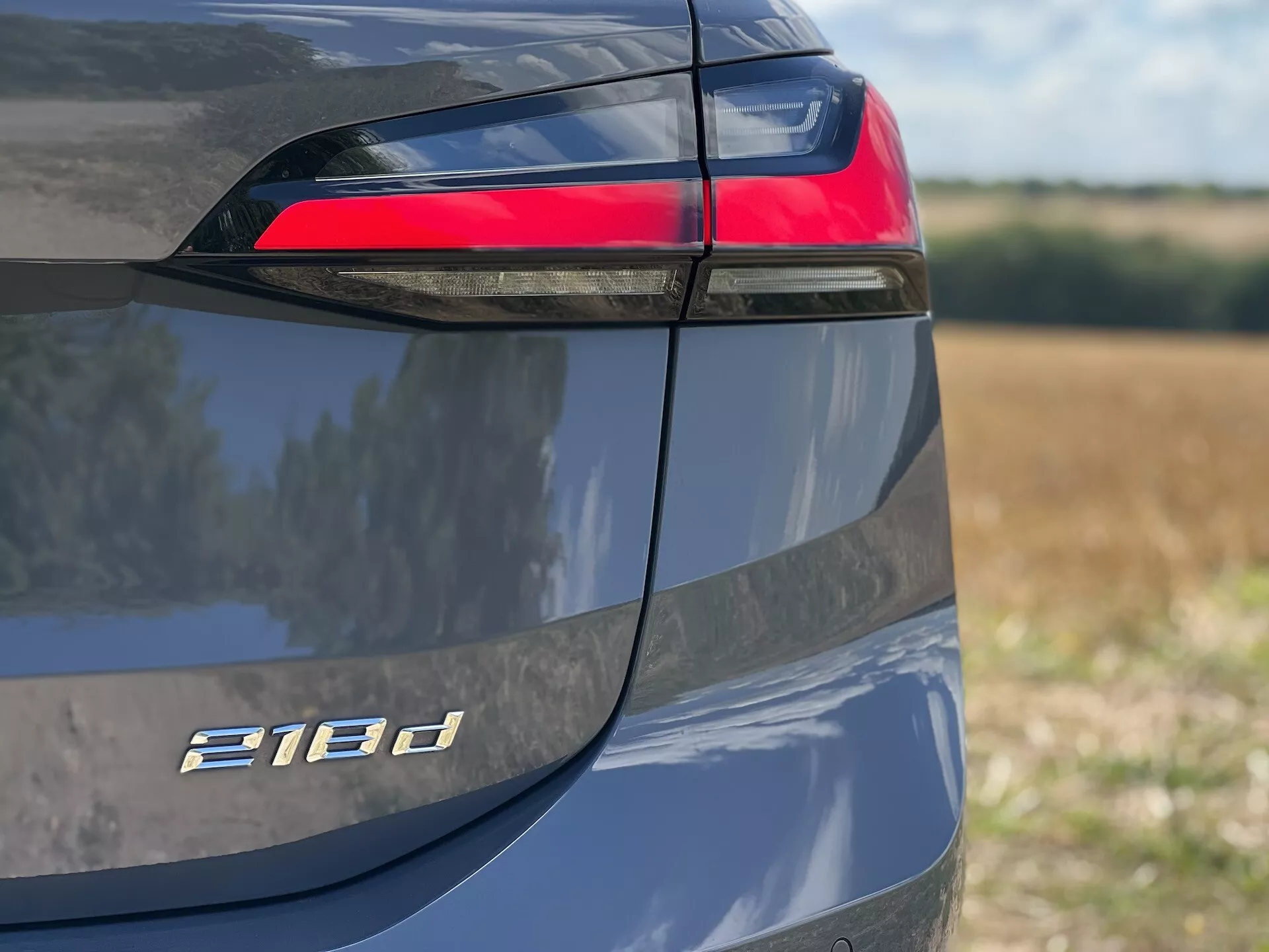 Podroben pogled na zadnjo levo stran BMW Serije 2 Active Tourer 218d s poudarkom na LED zopetnem lučnem grozdu, oznaki modela in kovinski barvni zaključek ob dnevni svetlobi
