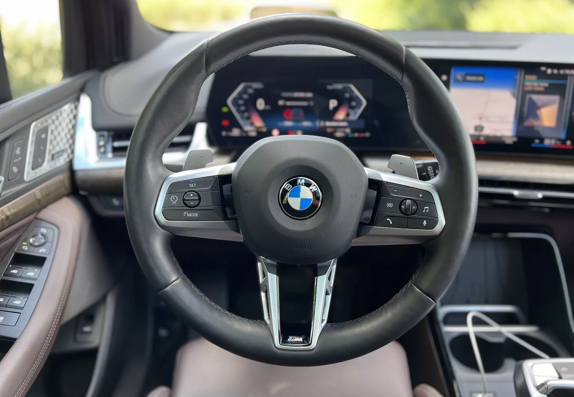 Pogled na notranjost BMW 2 Series Active Tourer 2022 iz perspektive voznika z vidnim volanom z logotipom BMW in oznako M, digitalnim merilnikom in delnim prikazovalnikom infotainment sistema, ki prikazuje napredno tehnologijo vozila in luksuzne značilnosti