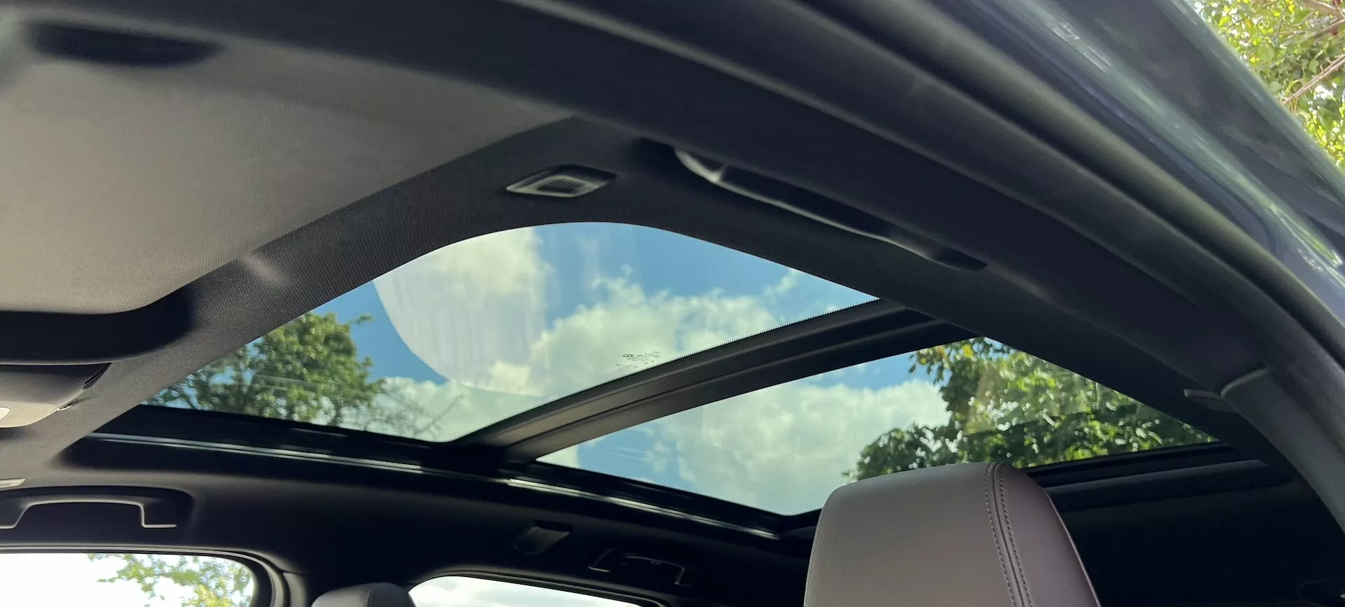 Notranji pogled na BMW serije 2 Active Tourer 2022 s delno odprtim panoramskim steklenim strešnim oknom in svetlimi notranjimi detajli, ki poudarjajo prostornost in luksuzne dodatke.