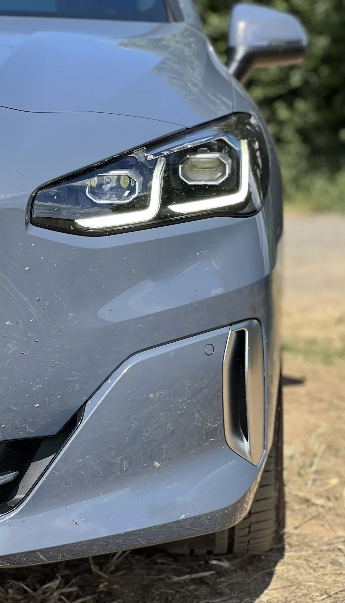 Pogled od blizu na sprednji levi del BMW serije 2 Active Gran Tourer 2022 z LED žarometom in aerodinamičnim odbijačem s parkirnim senzorjem, ki prikazuje napredno tehnologijo in oblikovanje.