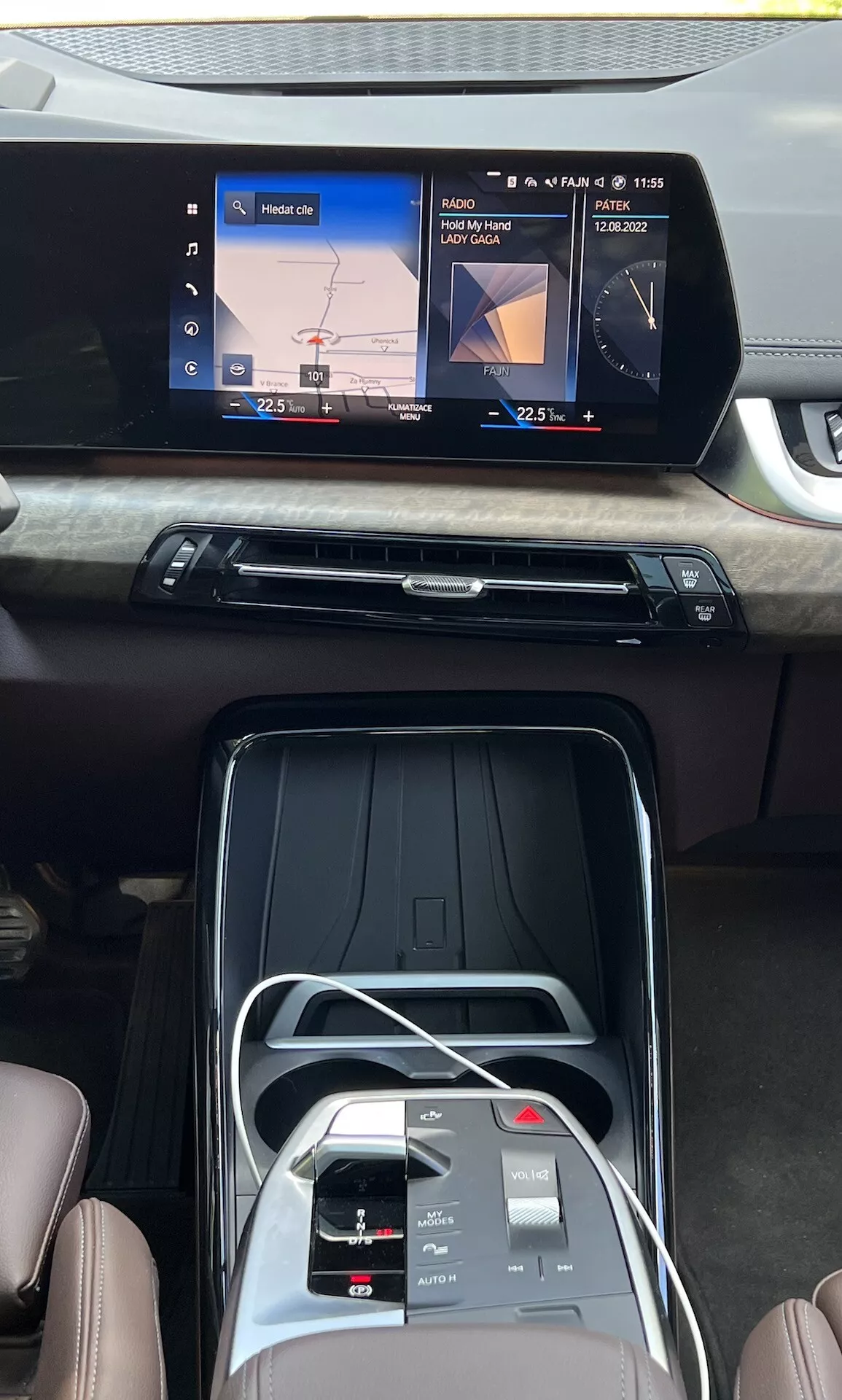 Notranji pogled na BMW serije 2 Active Grand Tourer 2022, ki prikazuje sredinsko konzolo, širokozaslonski zaslon na dotik z navigacijo in predvajanjem medijev, eleganten zračni vent z lesnim zaključkom, gumbe za nadzor klime, vmesnik na dotik, elektronski izbirnik prestav in sedeže iz premium usnja