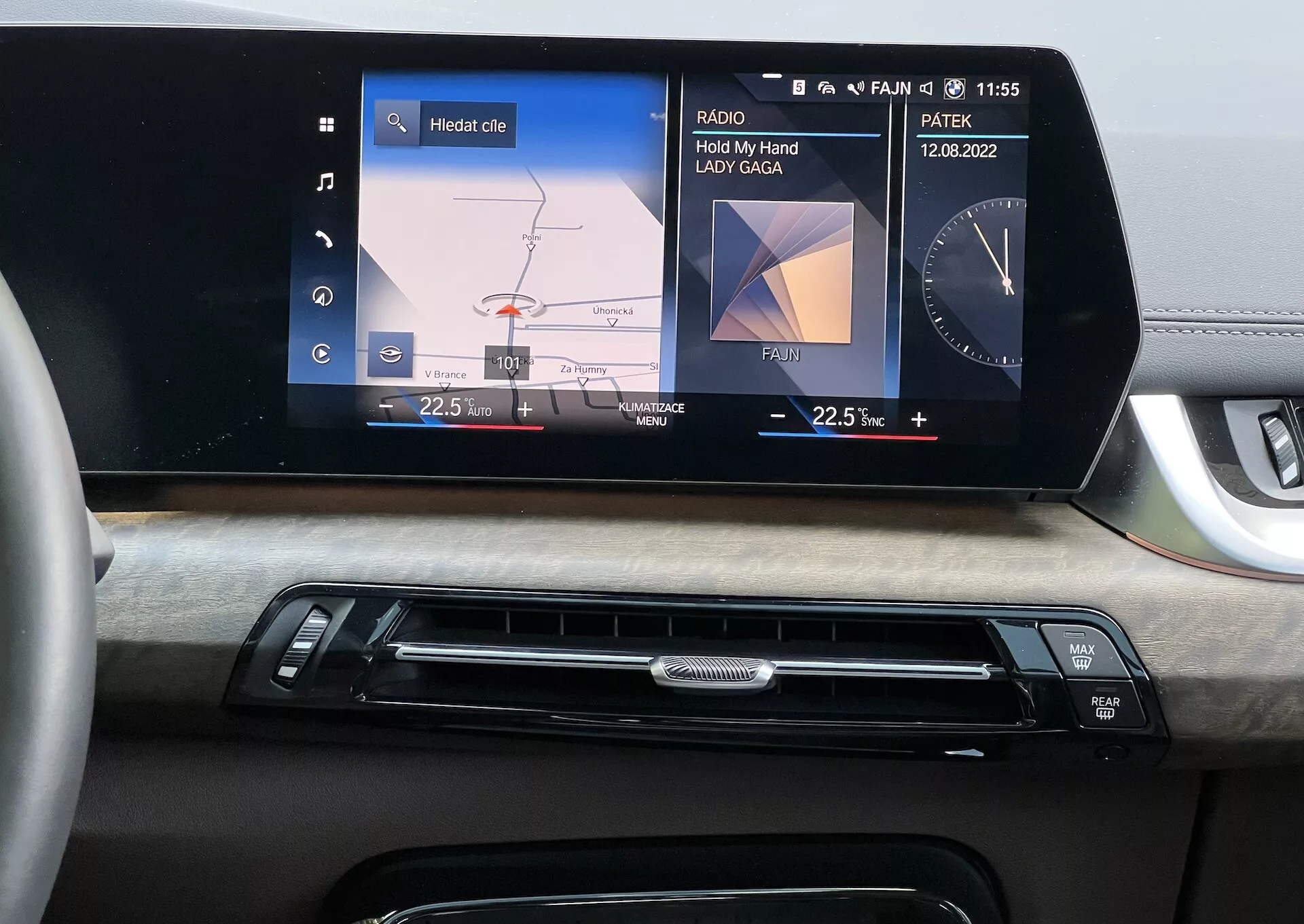 Notarni del BMW serije 2 Active Tourer 2022 s poudarkom na armaturni plošči s centralnim informacijsko-zabavnim sistemom, ki prikazuje grafični meni avtomobila za nastavitve žarometov in medijski zaslon ‘Hold My Hand’ od Lady Gaga, vidnost datuma in ure, dopolnjeno z leseno oblogo in gumbi za nadzor klime