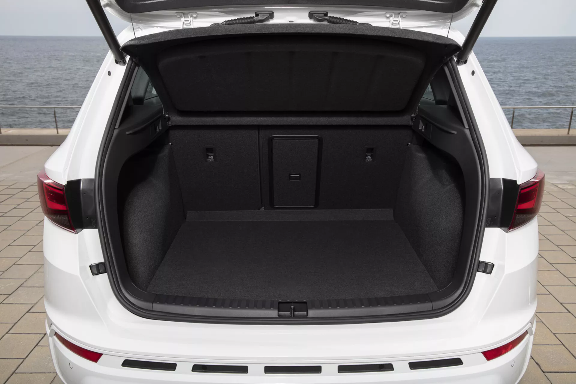 Zadnji pogled na beli SUV Cupra Ateca 2020 z odprtim prtljažnikom, ki prikazuje prostorno, čisto tovorno območje s ploskim tovornim dnom in temno notranjo preprogo, namigujoč na funkcije elektronsko upravljanega prtljažnih vrat in dizajn LED zadnjih luči.