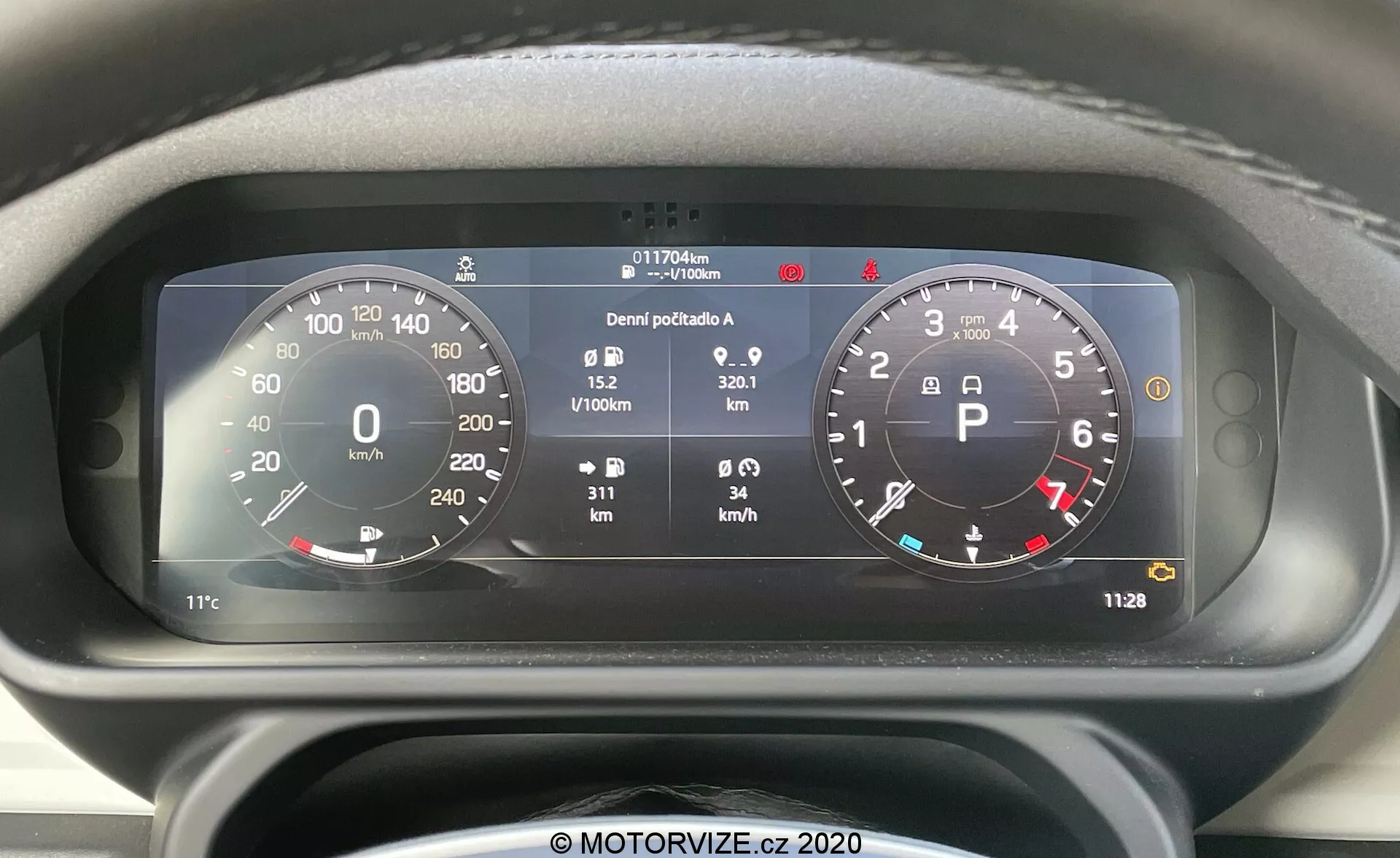 Od bližnje prikaz sprednjega pogleda na digitalni armaturni plošči Land Rover Defender 2020 z izrazitim krožnim merilnikom hitrosti (0-260 km/h) in merilnikom vrtljajev (0-8,000 RPM), integracijo različnih kazalnikov stanja vozila in podrobnimi informacijami, vključno z merilnikom goriva, temperaturo, števcem kilometrov (117,706 km), dnevnim števcem, povprečno porabo goriva (0.9 L/100km), povprečno hitrostjo (32.1 km/h) in digitalno uro (11:28).