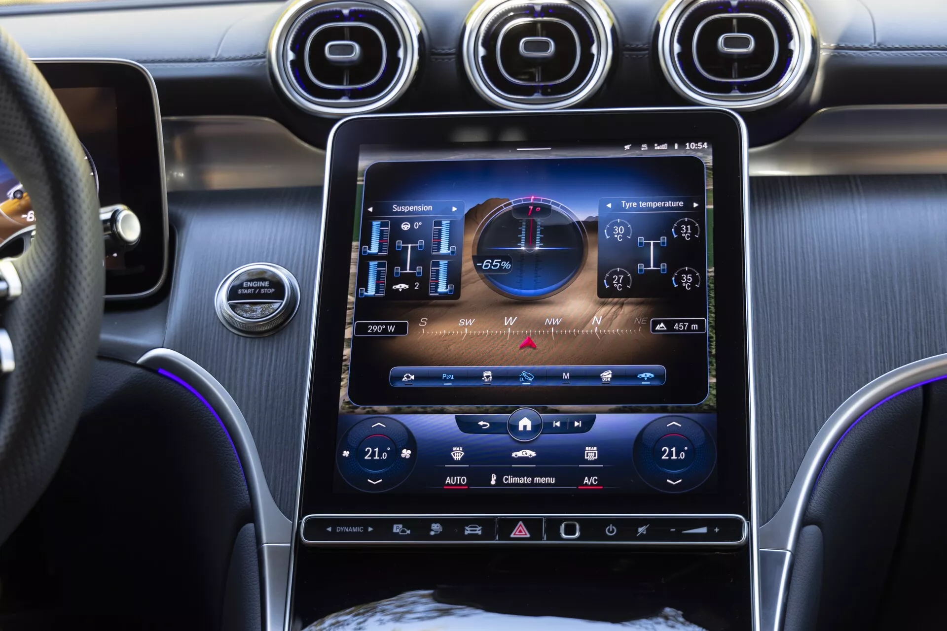 Pogled na sredinsko konzolo Mercedes GLC 2022 s pokončno nameščenim 10-12 palčnim zaslonom na dotik informacijsko-zabavnega sistema, ki prikazuje stanje vozila z digitalnim števcom hitrosti, tahometrom in nadzori klime, ki kažejo 21 stopinj Celzija za potnika in voznika. Razkošna notranjost vključuje zračne režice s kromiranimi poudarki, gumb za vžig izklopa motorja, večfunkcijski usnjen volan in modro ambientalno osvetlitev.