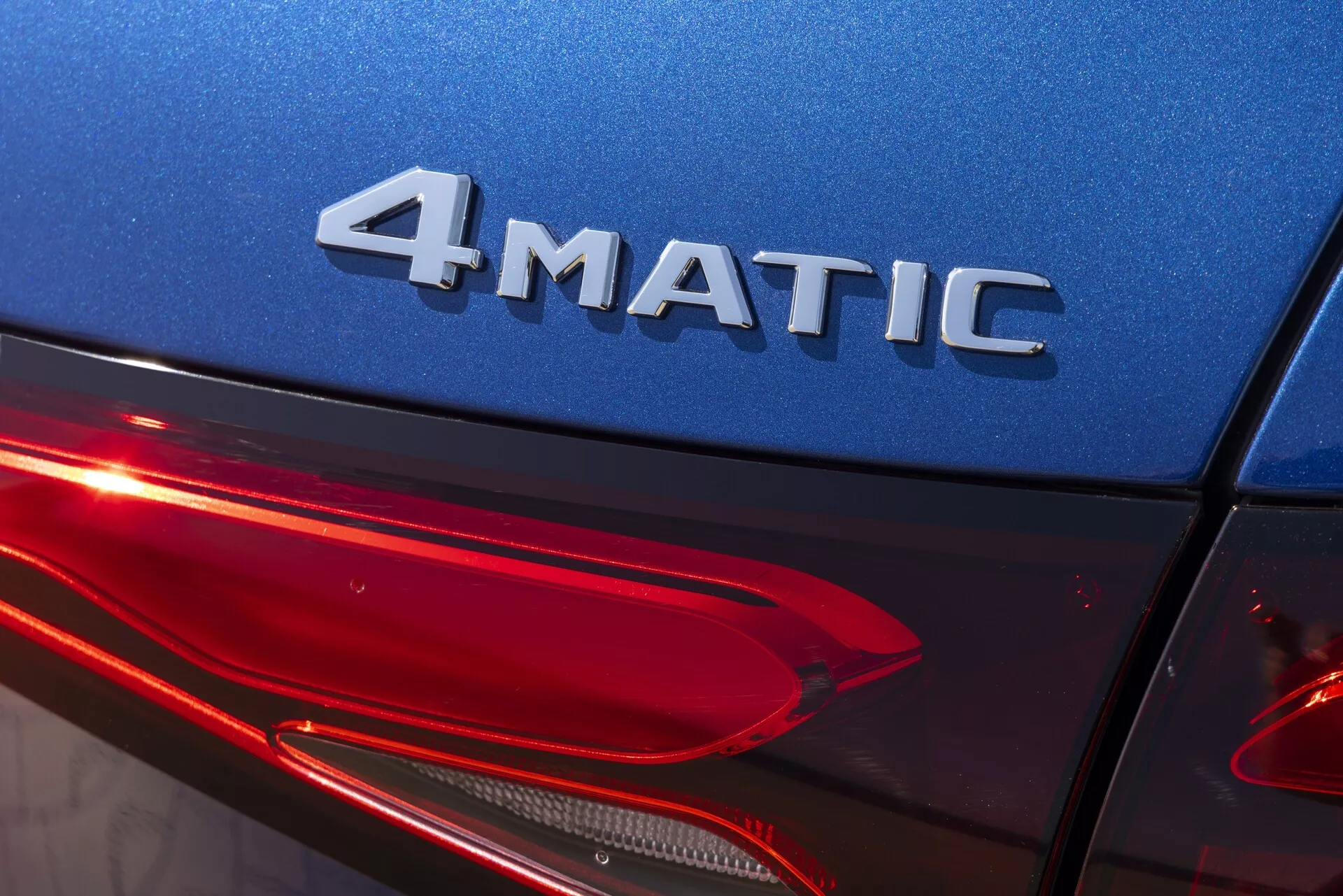 Bližnji posnetek zadnje četrtine Mercedesa GLC 2022 (254) pod rahlim kotom navzgor, ki prikazuje značko 4MATIC, sijajno modro karoserijo in modern dizajn zadnjih LED luči. Poudarek na tehnologiji štirikolesnega pogona, avtomobilski razsvetljavi in visokokakovostni zunanji obdelavi.