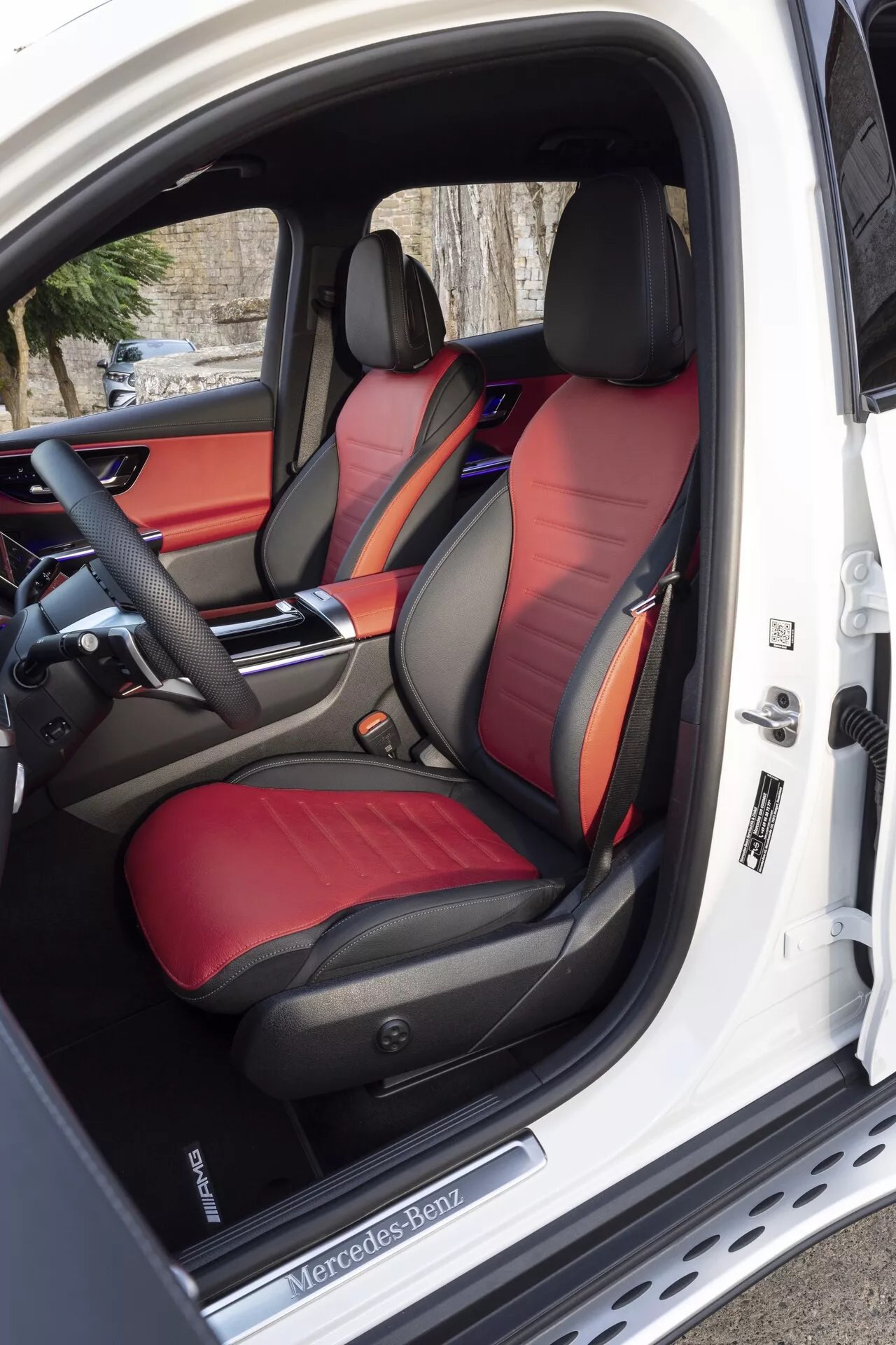 Notranji pogled na Mercedes-Benz GLC 2022, ki poudarja dvo-barvne športne sprednje sedeže z bleščečim usnjem, napreden nadzorni panel sedežev na odprtih voznikovih vratih ter deloma viden napreden multifunkcijski volan in elegantno armaturno ploščo z možnostjo prilagoditve ambientne osvetlitve.