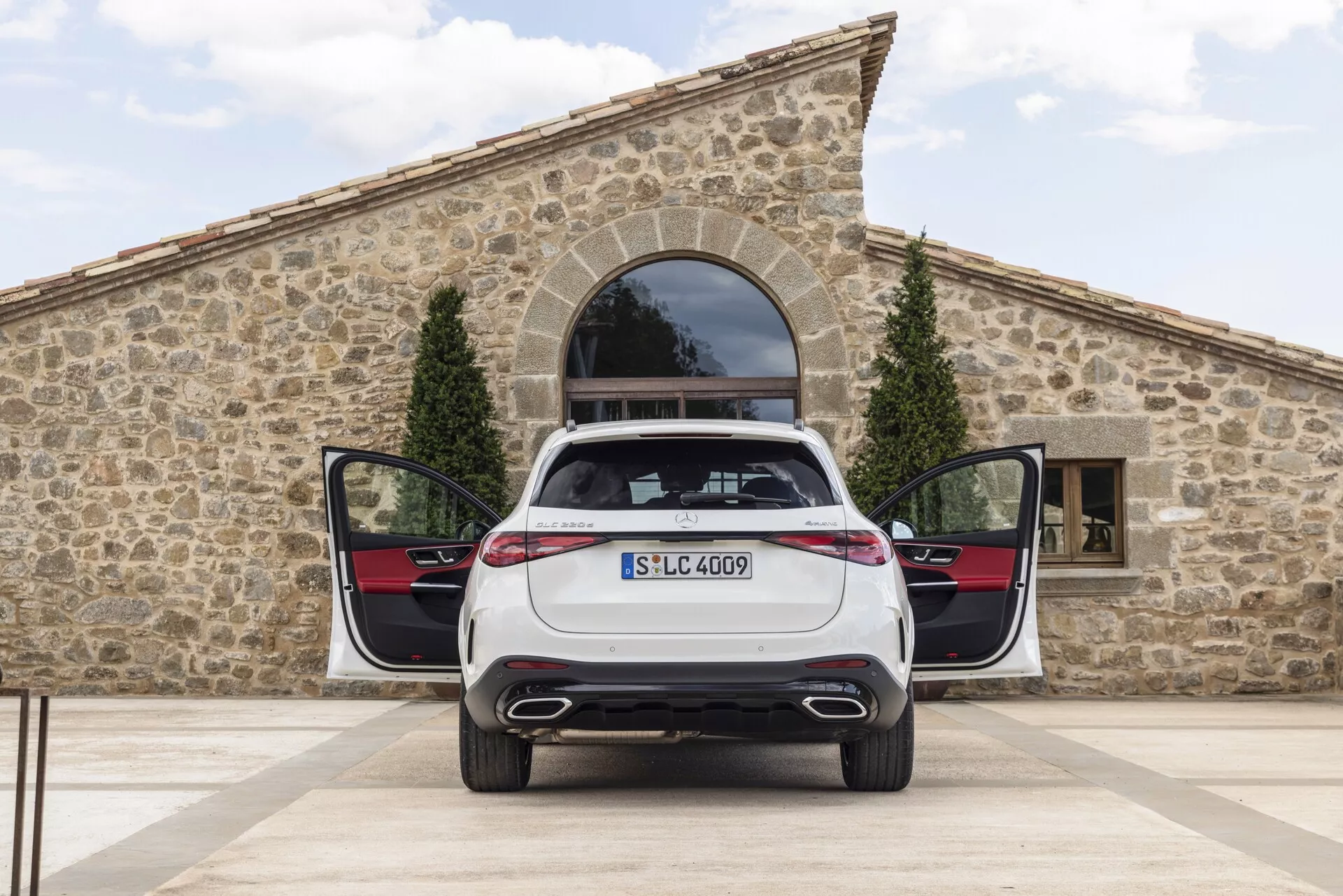 Pogled od zadaj na stoječi Mercedes GLC 2022 z odprtim prtljažnikom in rahlo odprtimi zadnjimi vrati, prikazuje dvojni izpušni sistem, elegantne LED zadnje luči, nameščeno registrsko tablico, značko modela in praktično ravno tovorno dno s premium notranjimi ploščami vrat z barvnim kontrastom in kovinskimi dodatki.