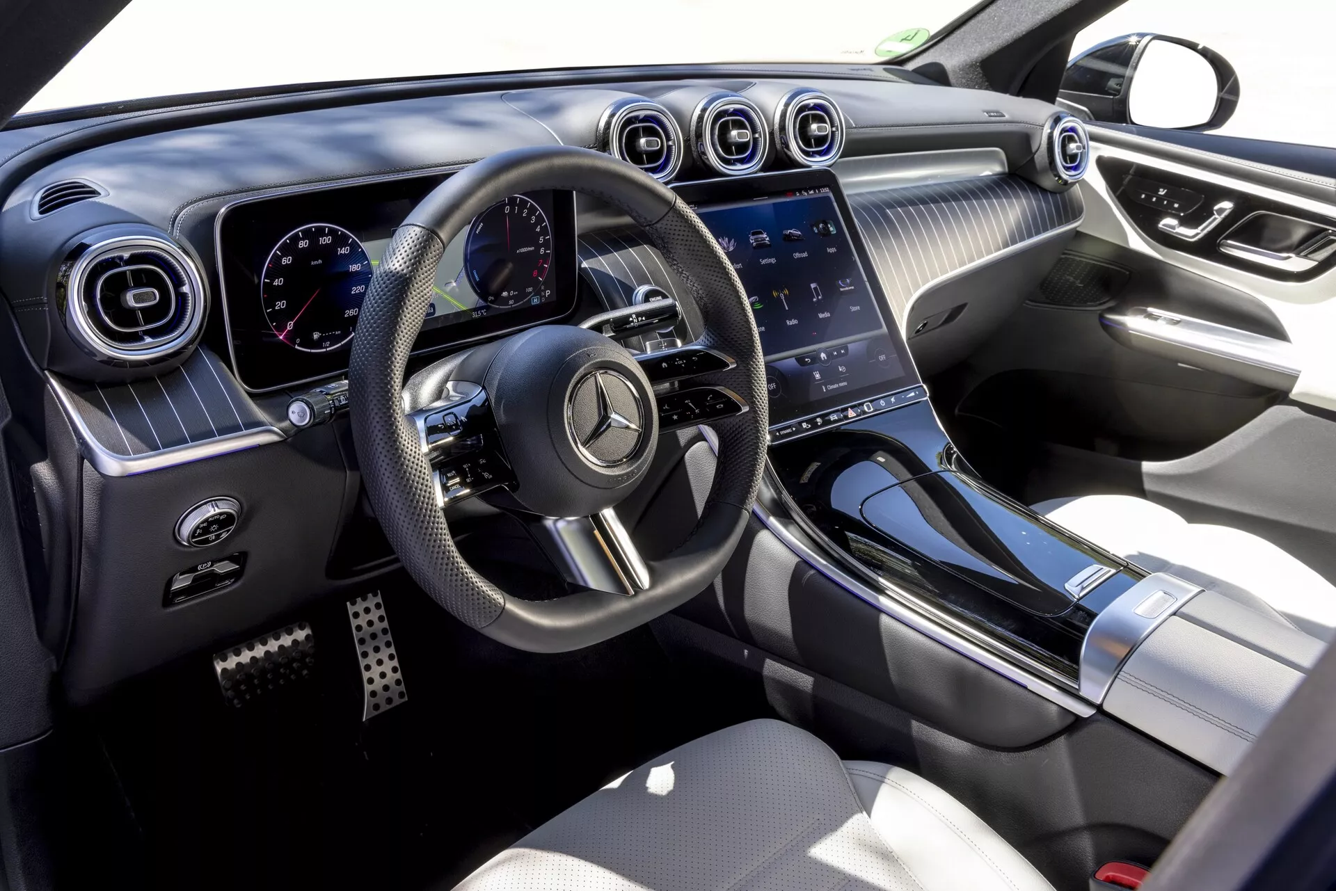 Pogled na notranjost Mercedes GLC 2022 (254) s potniške strani, ki poudarja sodoben in razkošen dizajn z večfunkcijskim volanom z ravnim dnom, digitalnim armaturnim prikazovalnikom, okroglimi prezračevalnimi odprtinami s kromiranimi poudarki, velikim zaslonom na dotik infotainment sistema in visokokakovostnimi materiali, kot so mehke površine, kovinski poudarki in usnjeni sedeži.