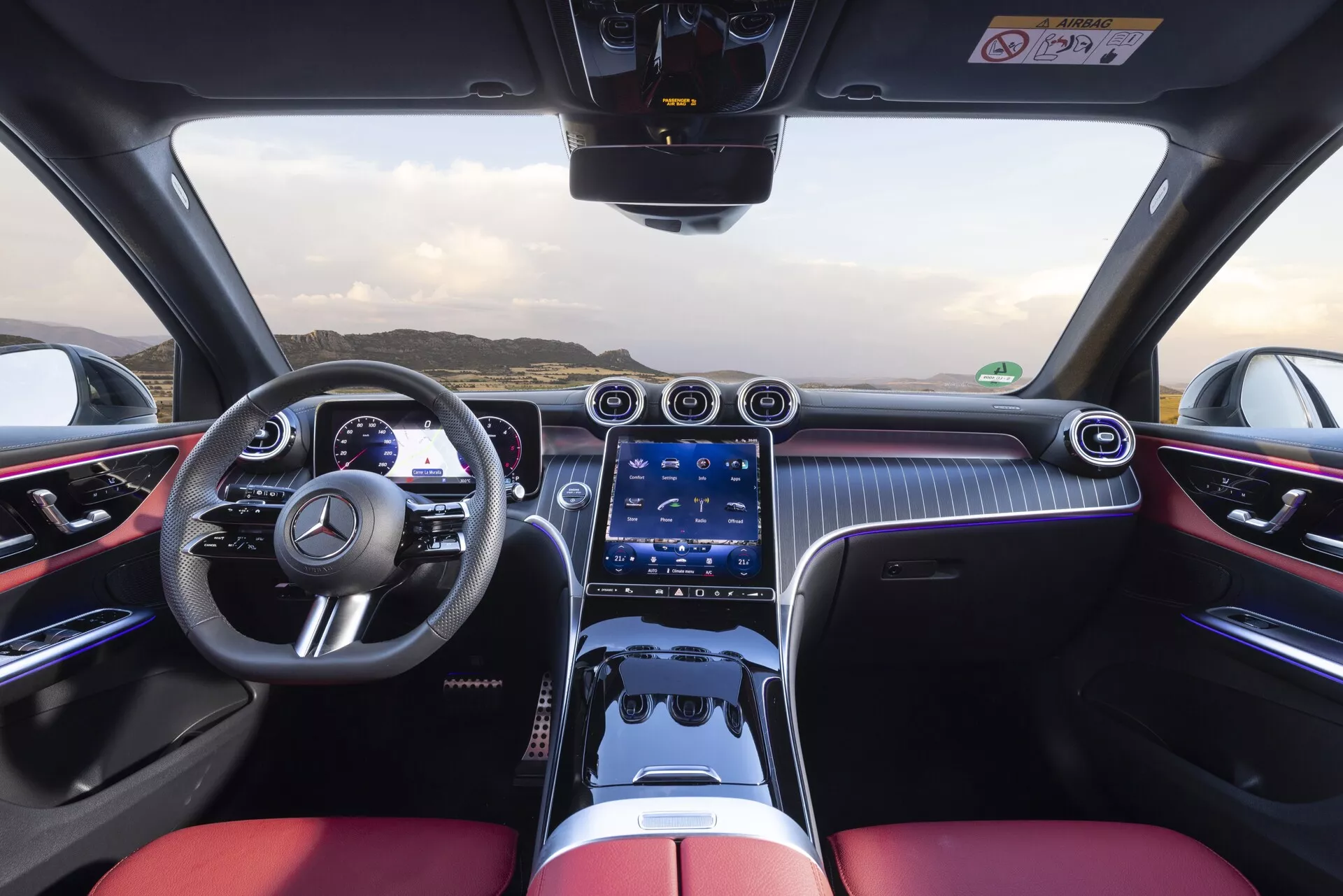 Pogled v notranjost Mercedes-Benz GLC 254 iz leta 2022 z vozniške perspektive, ki prikazuje športni volan z večfunkcijskimi gumbi, dvobarvno kabino s črnimi in živahnimi rdečimi luksuznimi sedeži, digitalni merilnik, širok zaslon na dotik infotainment sistema, kromirane zračnike, fizične gumbe za nadzor klime, vzorce, podobne karbonskim vlaknom, ambientalno osvetlitev, nadzor na dotik in visoko zmogljivo, luksuzno zasnovo.