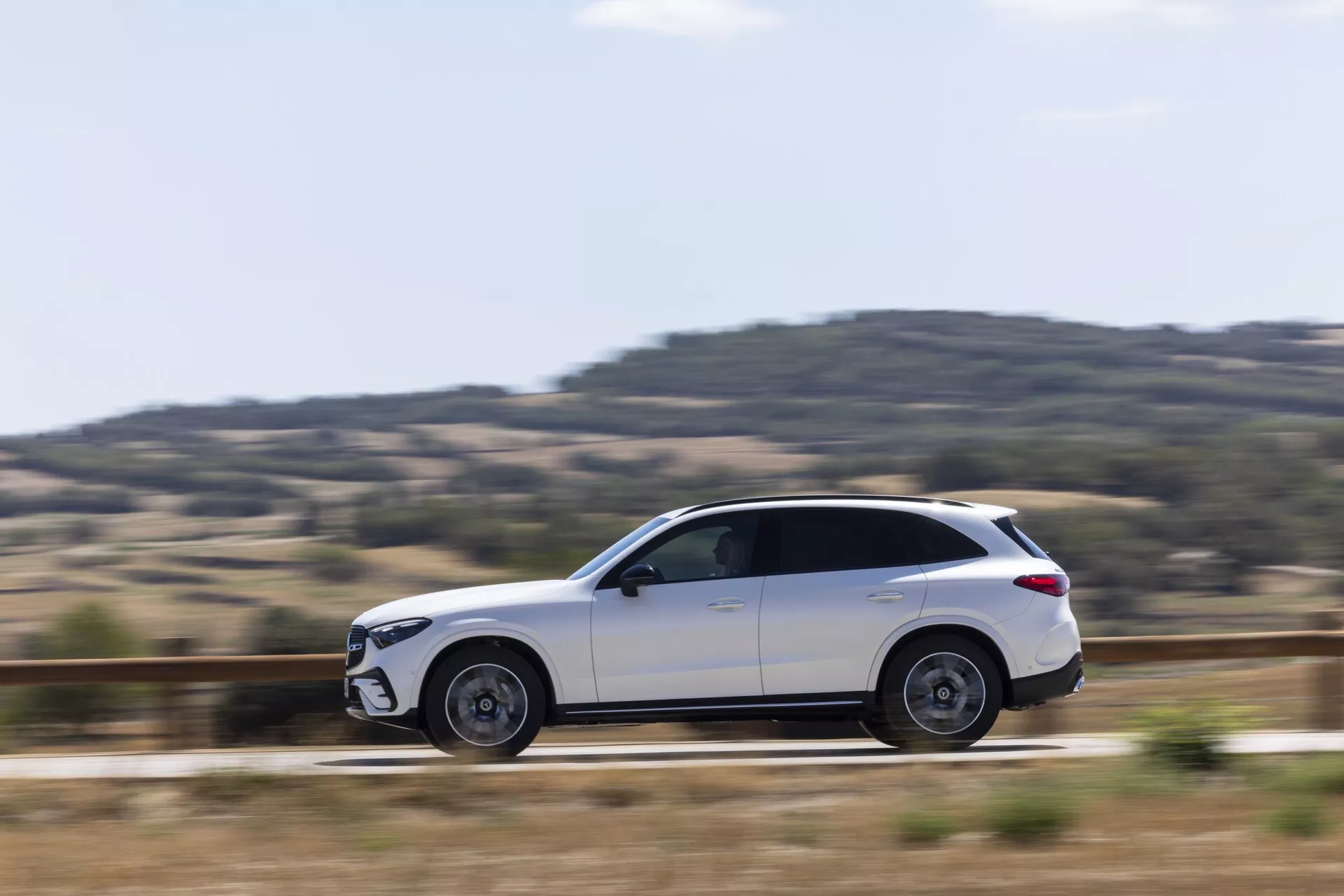 Bočni profilni pogled na bel Mercedes GLC 2022 SUV v gibanju, ki prikazuje elegantne oblikovalske linije, elegantno karoserijo s toniranimi okni, delno zamegljena aluminijasta platišča, stranska ogledala, vgrajene kljuke vrat, strešne nosilce in dobro uravnotežen kot kamere s tehniko panninga, ki poudarja dinamično gibanje vozila.