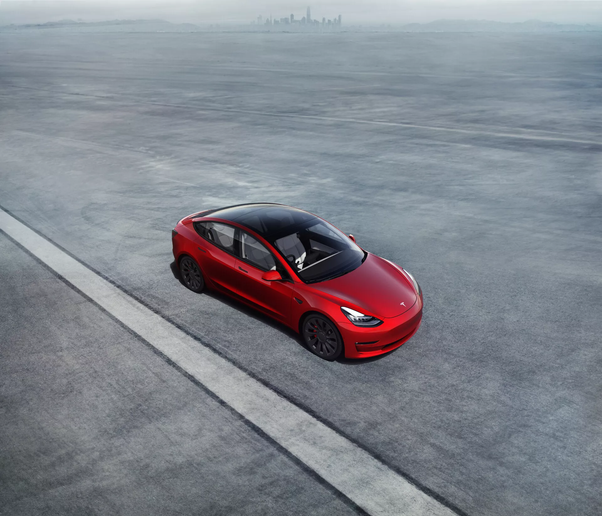 Zračni pogled na drzno rdeč Tesla Model 3 2019 (1. generacija), parkiran na ravni, sivi površini. Eleganten štirivratni limuzina ima aerodinamično silhueto, nagnjeno strešno linijo, ki se zlije v prtljažnik, ter edinstvena lita platišča. Vgrajeni ročaji vrat nakazujejo na aerodinamično učinkovitost. Visoka stopnja zatemnitve oken, odsotnost vidnega izpuha in moderne tanke luči nakazujejo napredno tehnologijo in potencialno električni ali hibridni pogonski sklop. Avto je postavljen vzporedno z ravno črto, kar poudarja urejeno postavitev.
