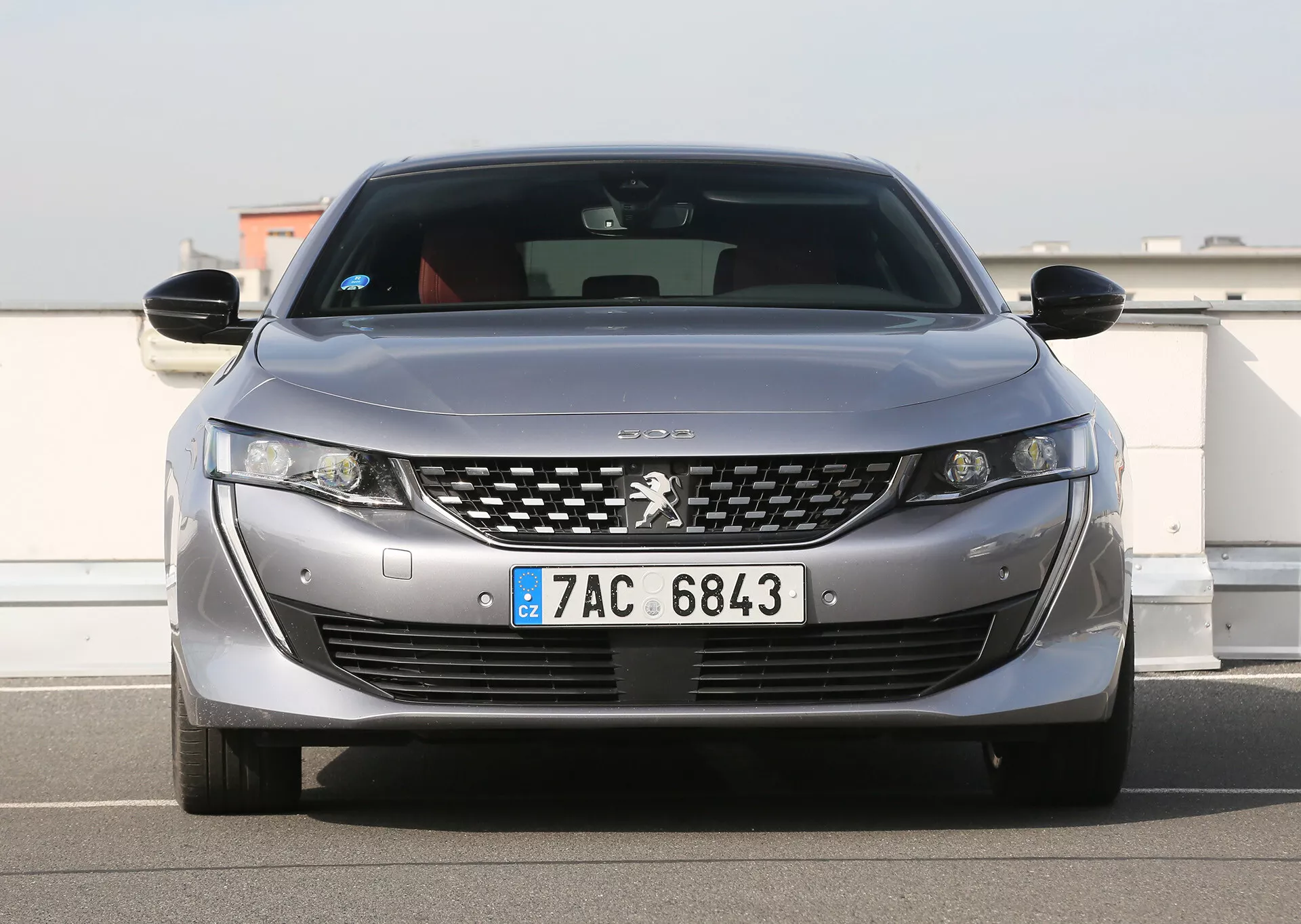 Sprednji pogled na srebrni Peugeot z LED žarometi, rešetko z kromiranimi detajli, parkirnimi senzorji in evropsko registrsko tablico, prikazuje sodobne oblikovne in tehnološke značilnosti, parkiran na prostem pod jasnim nebom