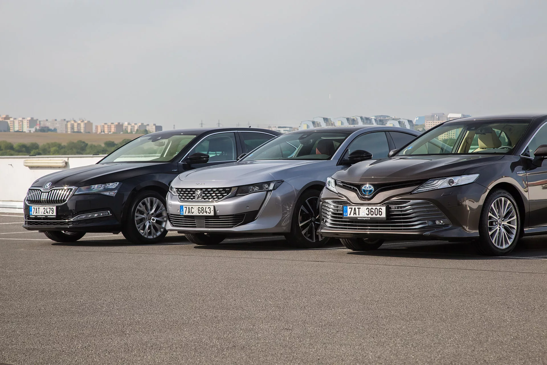 Tri limuzine Toyota Camry, modelno leto 2001, parkirane ena ob drugi na zunanjem parkirišču, obrnjene v levo s čistim pogledom na njihove moderne sprednje rešetke, žaromete in aerodinamične zasnove