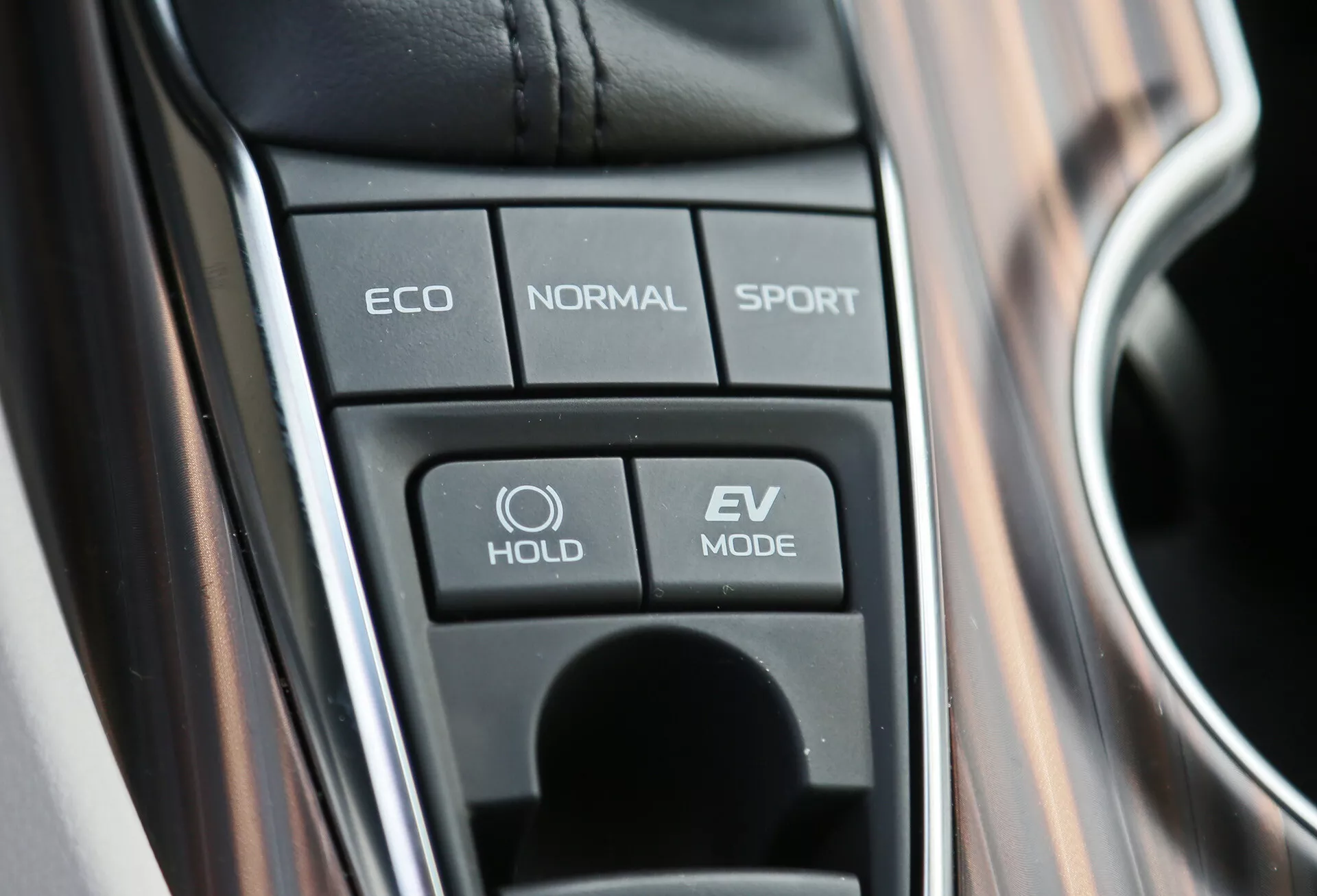 Pogled od blizu na sredinsko konzolo Toyota Camry 2001 s tipkami za izbiro načina vožnje, vključno z ECO, NORMAL, SPORT, funkcijo HOLD in načinom EV, kar poudarja napredne tehnologije vozila in hibridne zmožnosti.