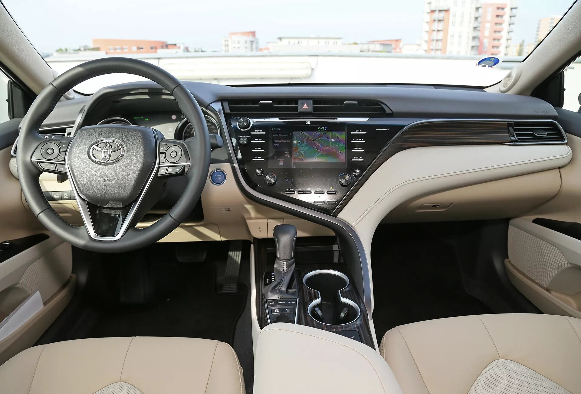 Pogled na notranjost limuzine Toyota Camry 2001, s poudarkom na moderni dvobarvni bež in črni armaturni plošči z vgrajenim zaslonom na dotik, multifunkcijskim volanom in podrobnim kokpitom iz perspektive zadnjega srednjega sedeža.