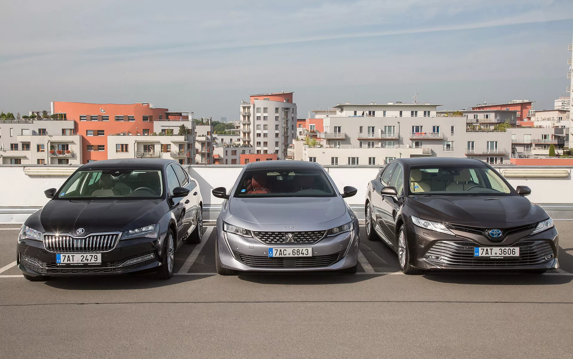Primerjava limuzin Skoda, Peugeot in Toyota drug ob drugu v pogledu s treh četrtin spredaj na parkirišču na strehi, poudarjajoč moderne oblikovne značilnosti, kot so LED osvetlitev, aerodinamične oblike in kromirani poudarki