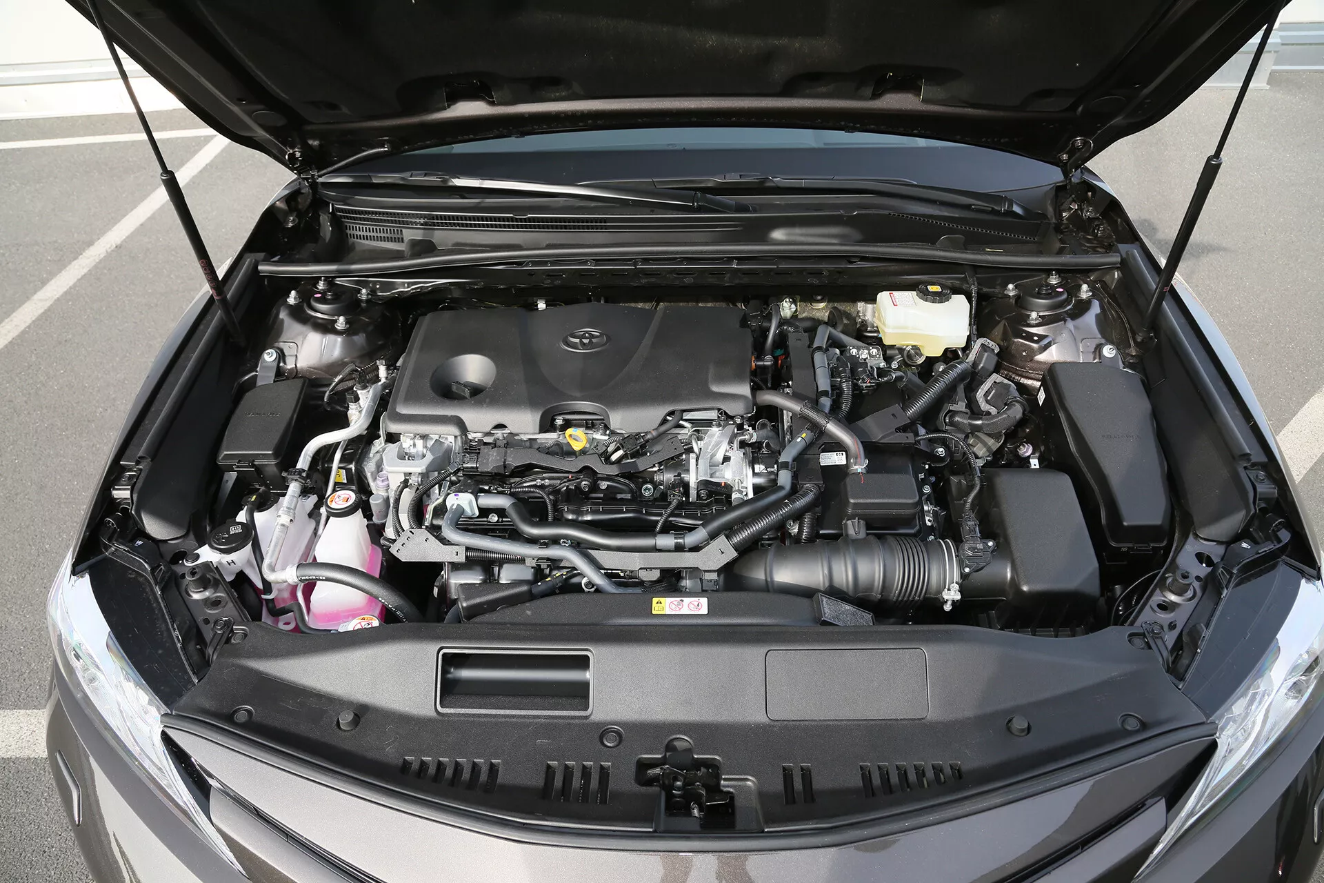 Podroben pogled na motorični prostor limuzine Toyota Camry letnik 2001 z odprtim pokrovom, ki prikazuje sodobno zasnovo motorja, vidno zračni dovod, rezervoar za zavorno tekočino, elektronske napeljave in komponente hladilnega sistema