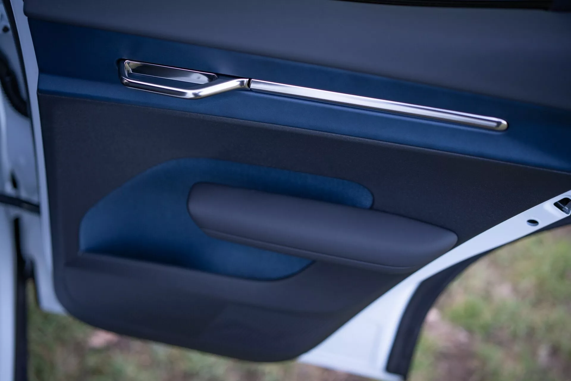 Posnetek od blizu notranjosti vrat avtomobila Volvo EX30 2024, ki prikazuje elegantno kovinsko kljuko vrat, ergonomski naslon za roke in shrambni žep v temni, visokokakovostni izvedbi