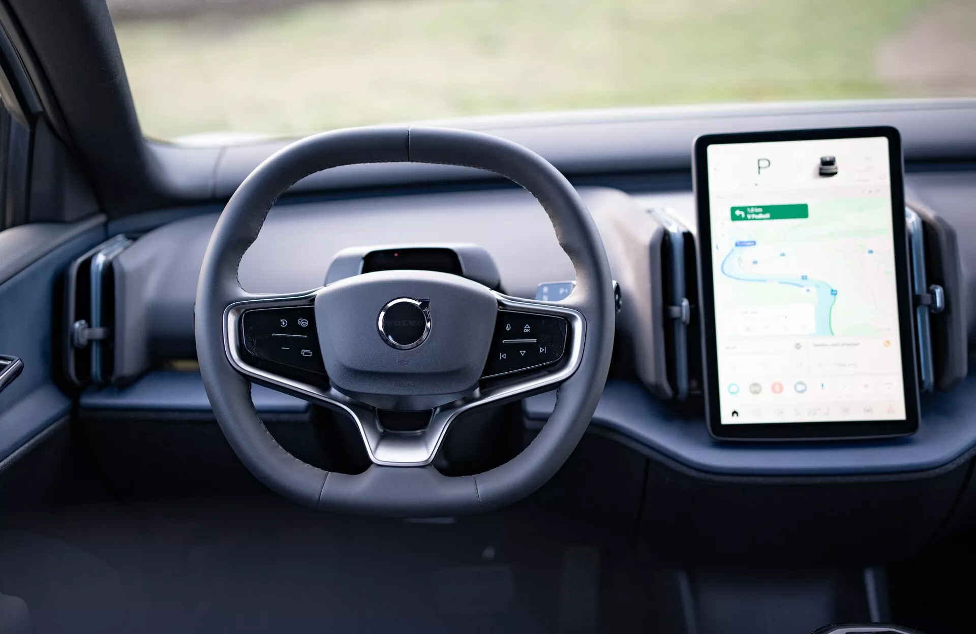 Notranji pogled na Volvo EX30 2024, ki prikazuje sodobno obliko volana in digitalne merilnike na armaturni plošči, vključno z GPS omogočenim navpično usmerjenim zaslonom na dotik za informacijsko-zabavni sistem.