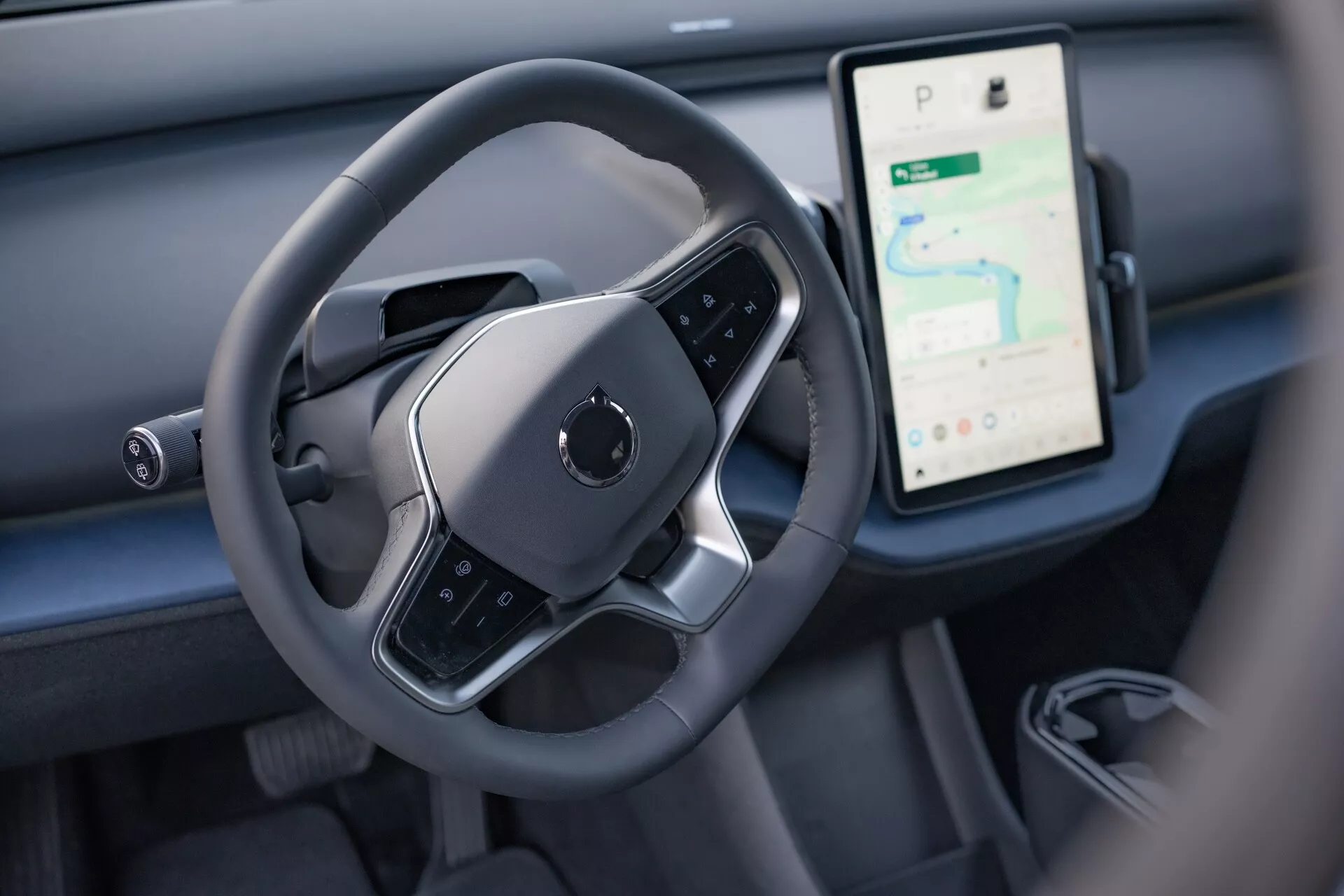 Pogled notranjosti Volvo EX30 2024, ki poudarja območje nadzora voznika s sodobnim volanom z ravnim dnom in velikim navpičnim zaslonom na dotik za navigacijo in medije na armaturni plošči