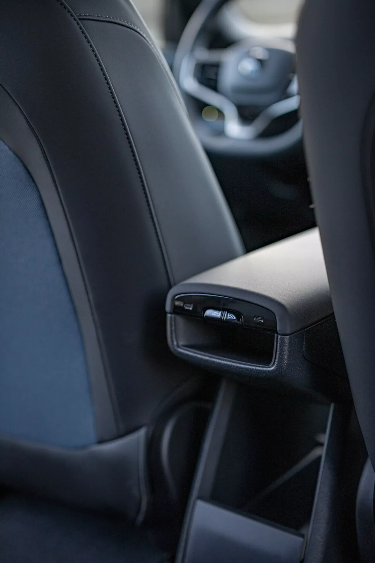 Notranji pogled na Volvo EX30 2024, osredotočen na podrobne značilnosti zadnje sredinske konzole iz perspektive srednjega zadnjega potnika, vključno z USB vrati in zračnimi režami, ki prikazujejo razkošje in tehnologijo