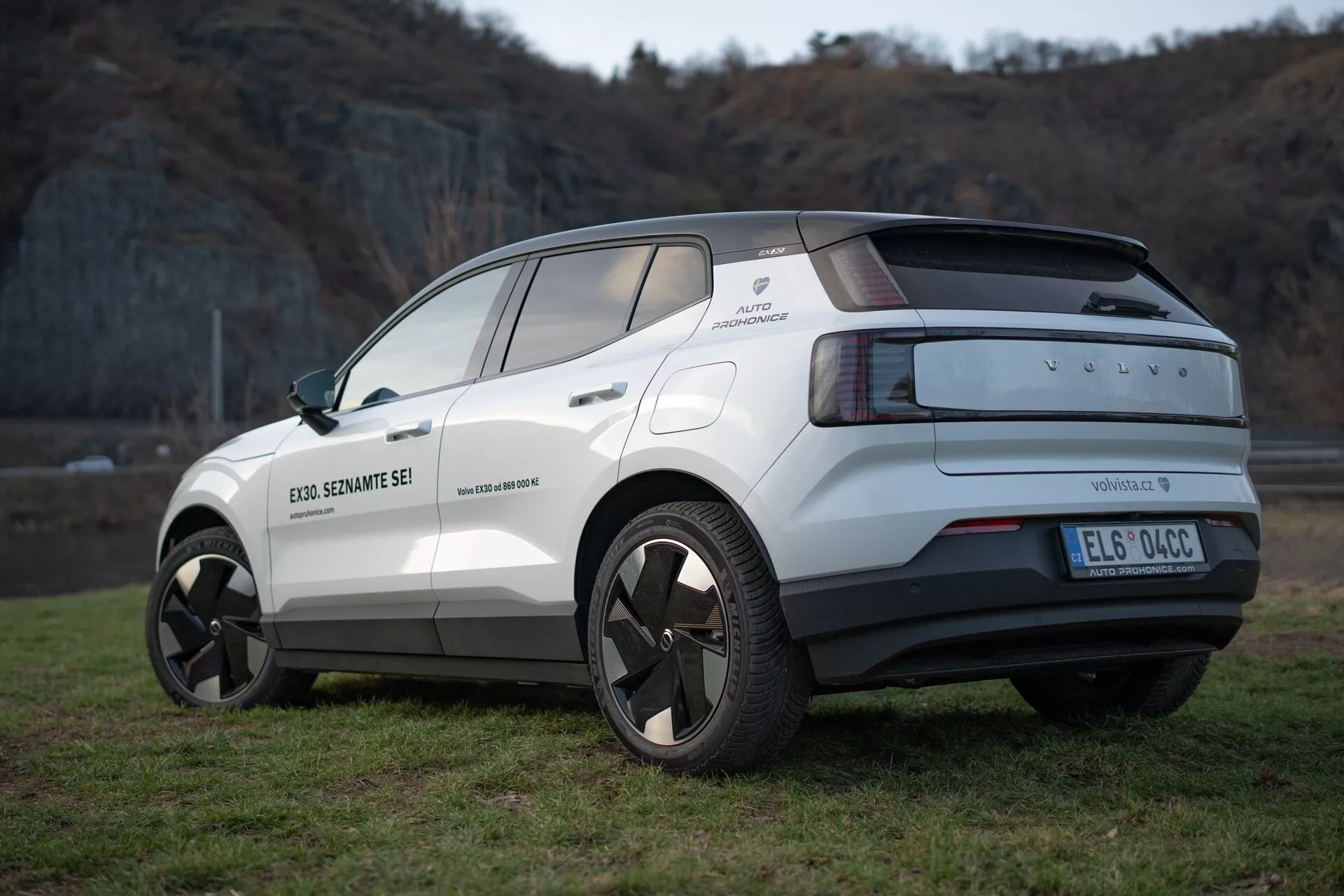 Zadnji tričetrtinski pogled na električni križanec Volvo EX30 letnik 2024 v beli barvi, ki poudarja njegov sodoben dizajn, lita platišča, senzorje za parkiranje in funkcije pomoči vozniku