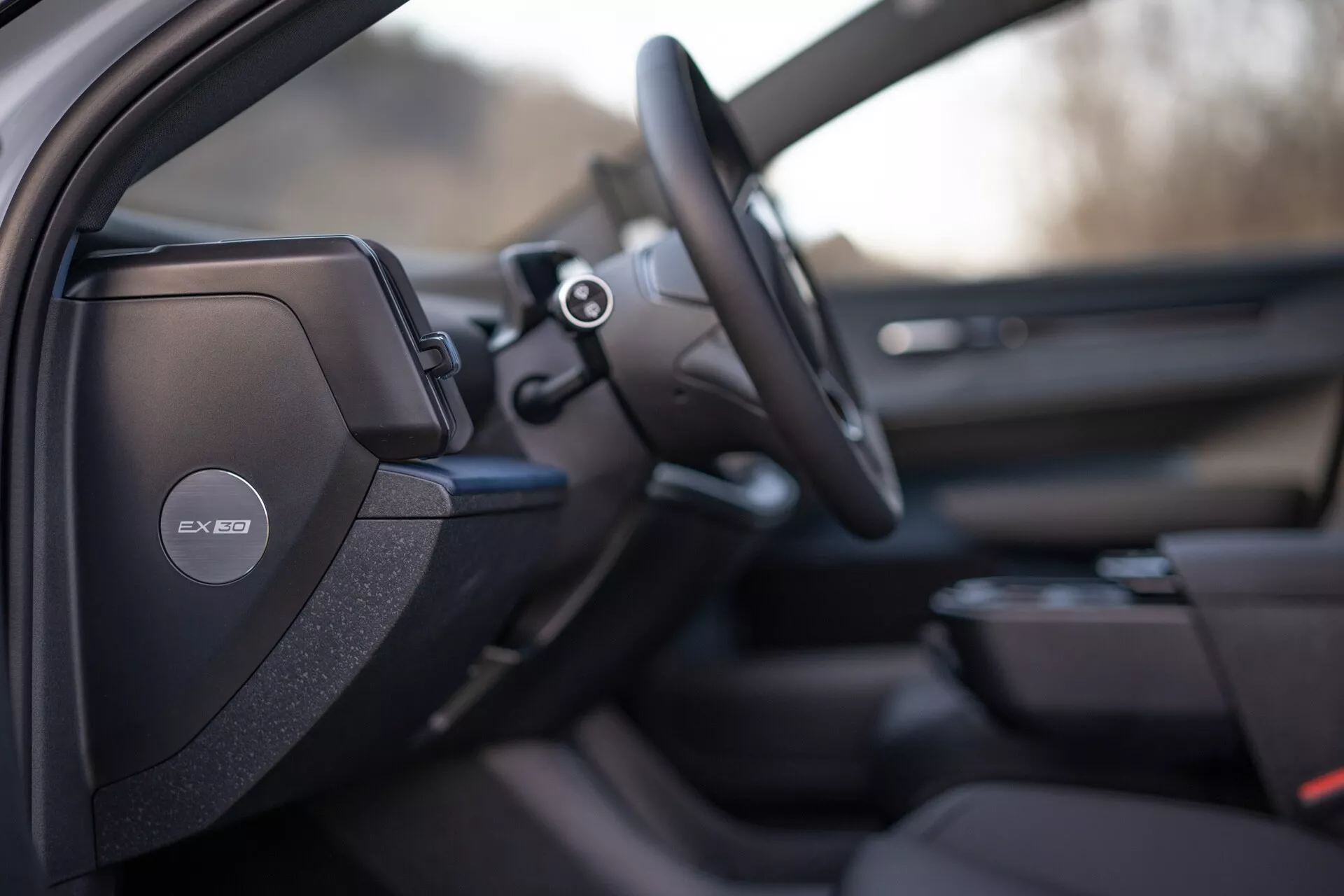Notranji pogled na Volvo EX30 2024, osredotočen na voznikovo stran, s podrobno športno ali premijsko zasnovo sedeža, zvočnim sistemom Harman Kardon na B-stebričku, večfunkcijskim volanom in namigi naprednega informacijsko-zabavnega sistema in oblikovanja panela vrat sopotnika