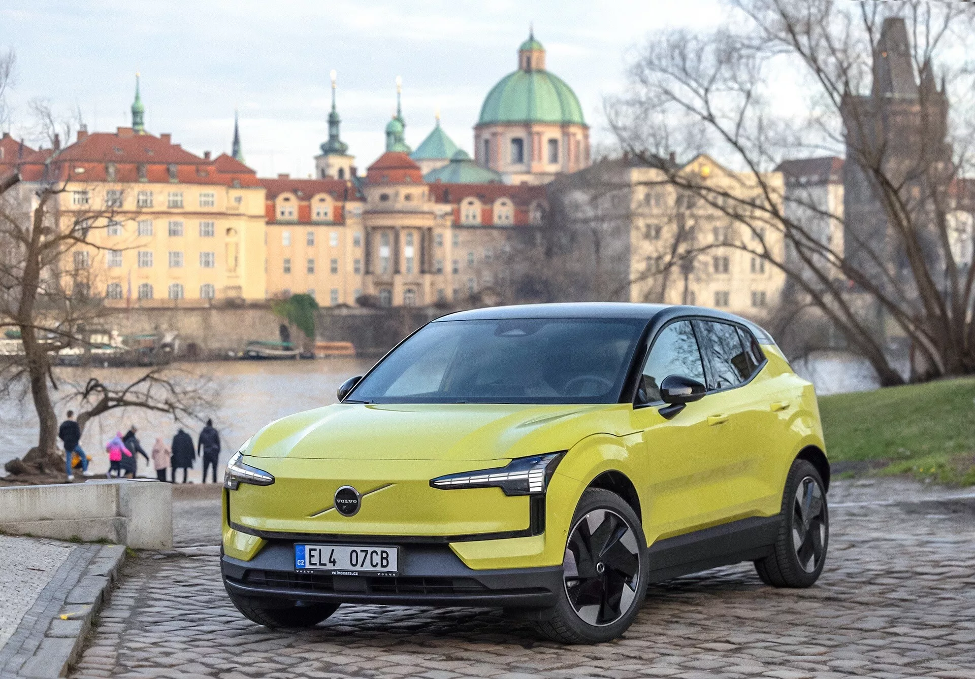 Limonino zeleni Volvo EX30 2024, pogled s sprednje strani pod kotom tri četrtine na tlakovcih, z modernimi LED žarometi in značilnostmi električne zasnove, urbano evropsko ozadje