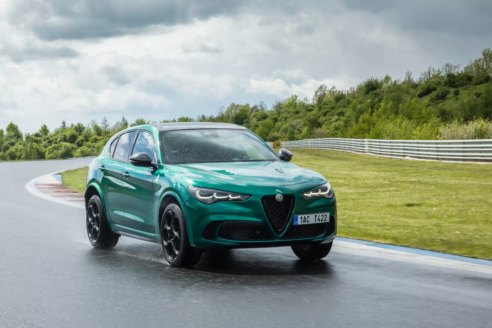 Alfa Romeo Giulia Quadrifoglio 2023 v gibanju na mokri dirkaški stezi, prikazuje aerodinamično oblikovanje z velikimi zračnimi vhodi, agresivnimi LED žarometi in metalno zeleno barvo z mat črnimi platišči z več kraki.