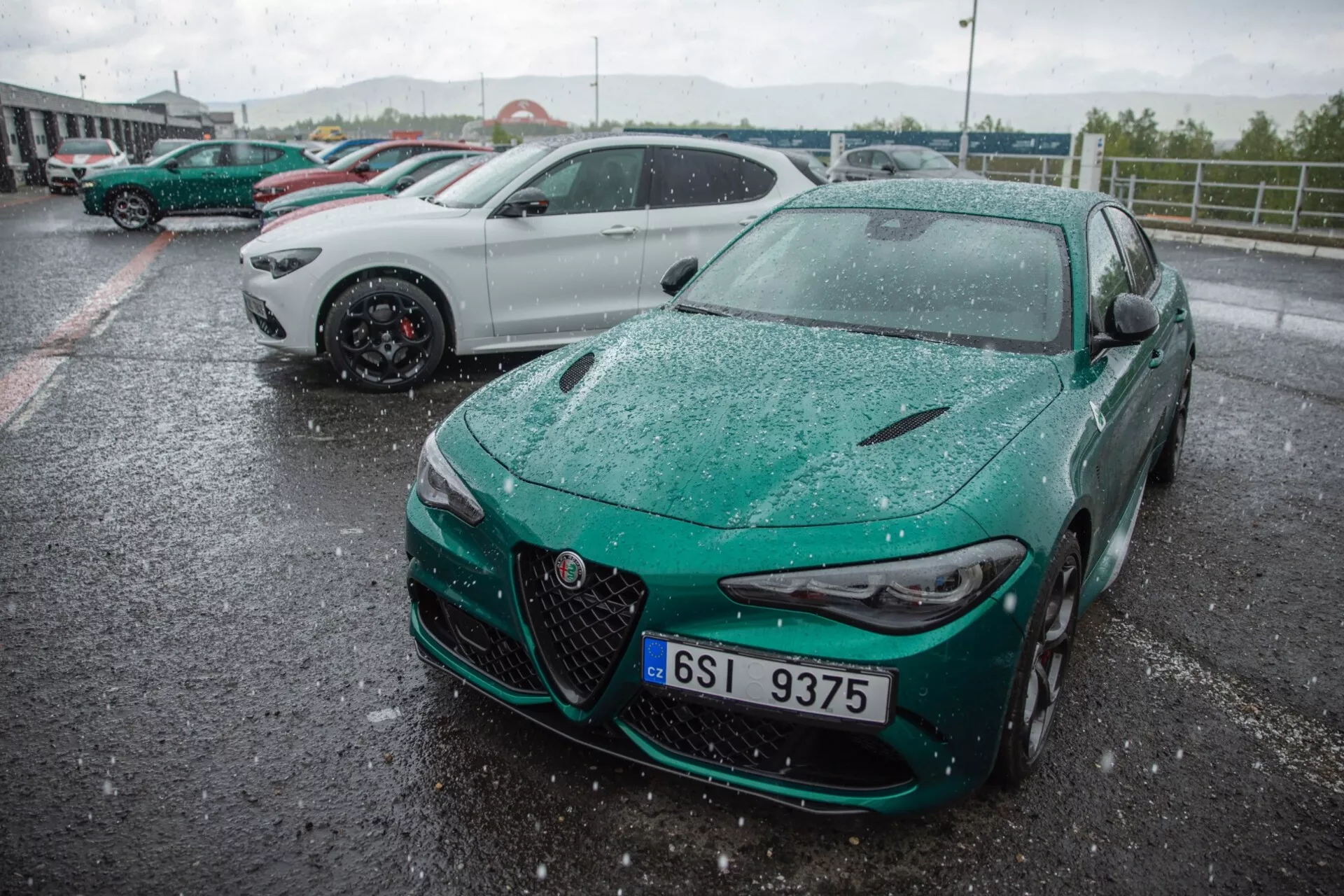 Alfa Romeo Giulia Quadrifoglio 2023, posneta iz sprednjega tričetrtinskega kota, ki prikazuje športno oblikovanje, izstopajočo masko z osrednjim znakom, vitke LED žaromete in aerodinamični sprednji odbijač v deževnem zunanjem okolju