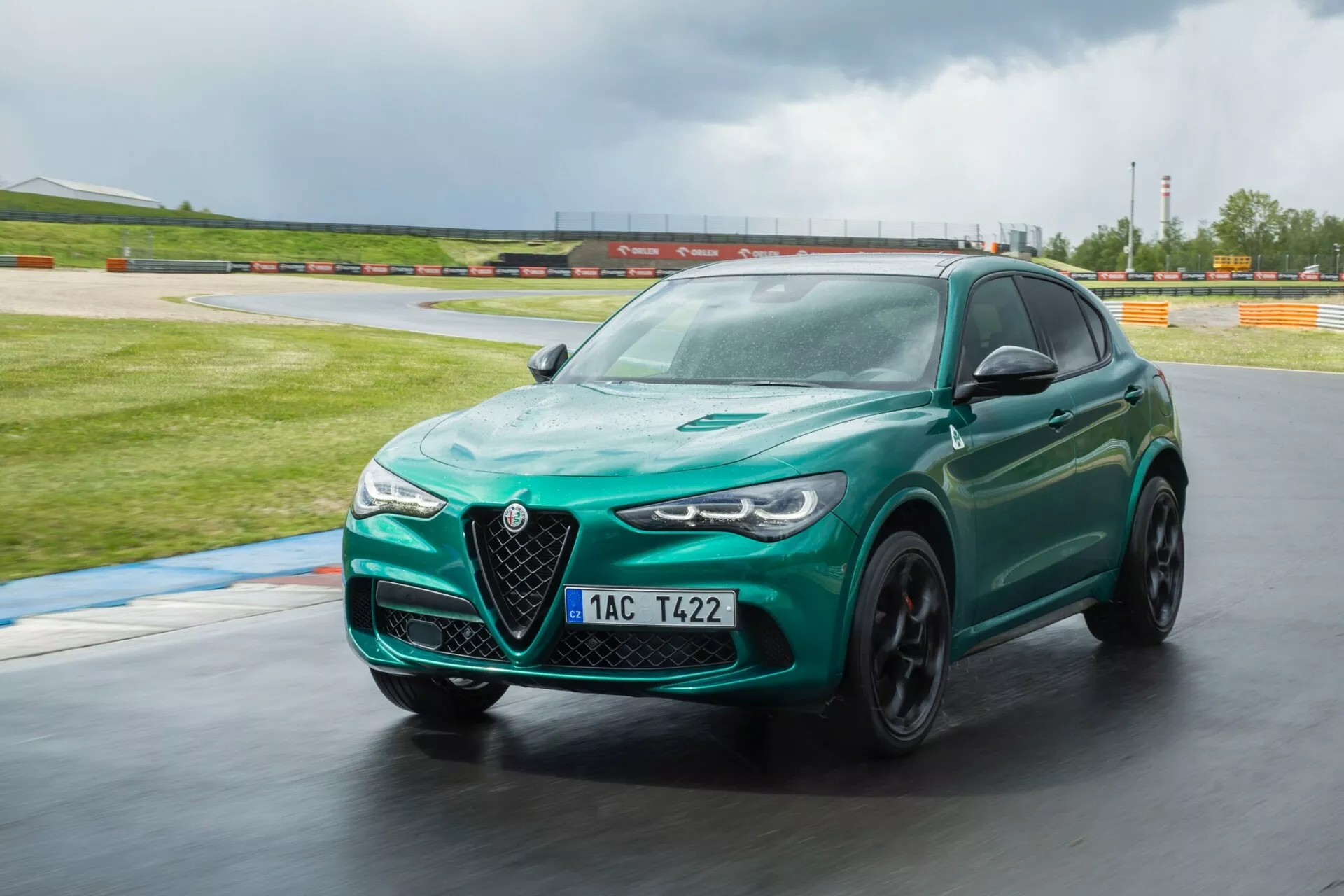 Alfa Romeo Giulia Quadrifoglio 2023 v metalik zeleni, dinamično zavija na dirkališču, poudarjeno z agresivno sprednjo fasado, elegantnimi LED žarometi in športno držo, podkrepljeno s tehnološkimi značilnostmi kot so napredna aerodinamika in zavorne zmogljivosti visokih zmogljivosti.