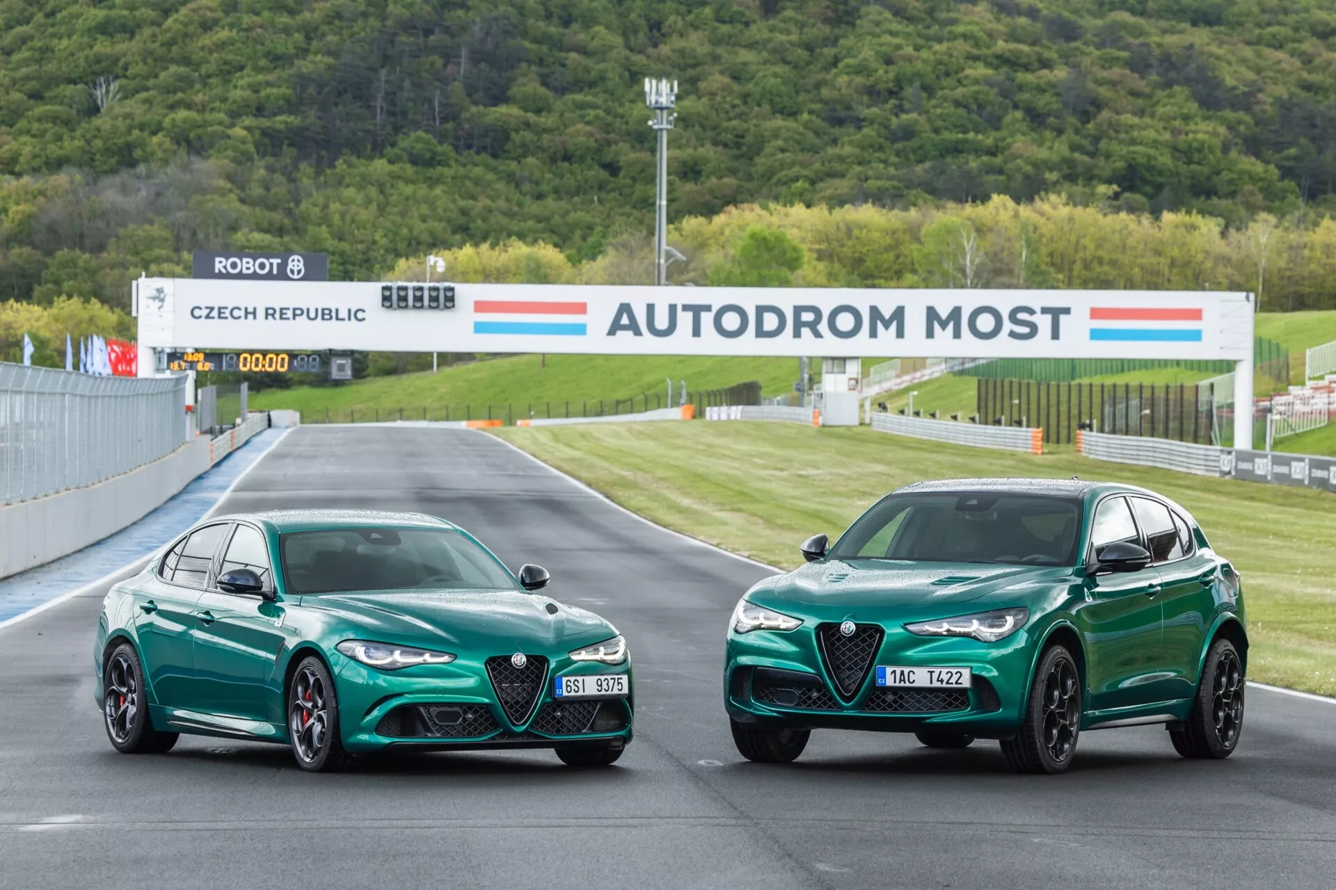 Alfa-Romeo Giulia Quadrifoglio in model SUV iz leta 2023, parkirana na dirkališču, s prikazom sprednjih in stranskih profilov z osredotočenjem na zmogljivostne lastnosti, kot so aerodinamična oblika, LED žarometi in značilna zelena barva pod profesionalno dirkališko razsvetljavo