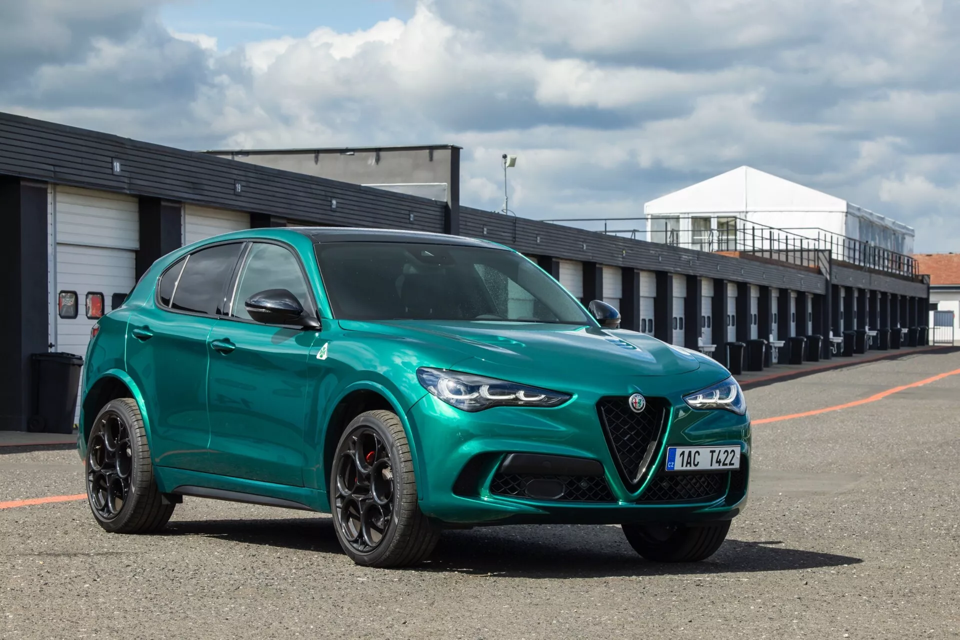 Alfa Romeo Giulia Quadrifoglio 2023 v metalik zeleni z značilno ščitno obliko rešetke in elegantnimi LED žarometi, fotografirano iz kota tri četrtine spredaj, poudarja športne in razkošne oblikovalske značilnosti na dirkališču.