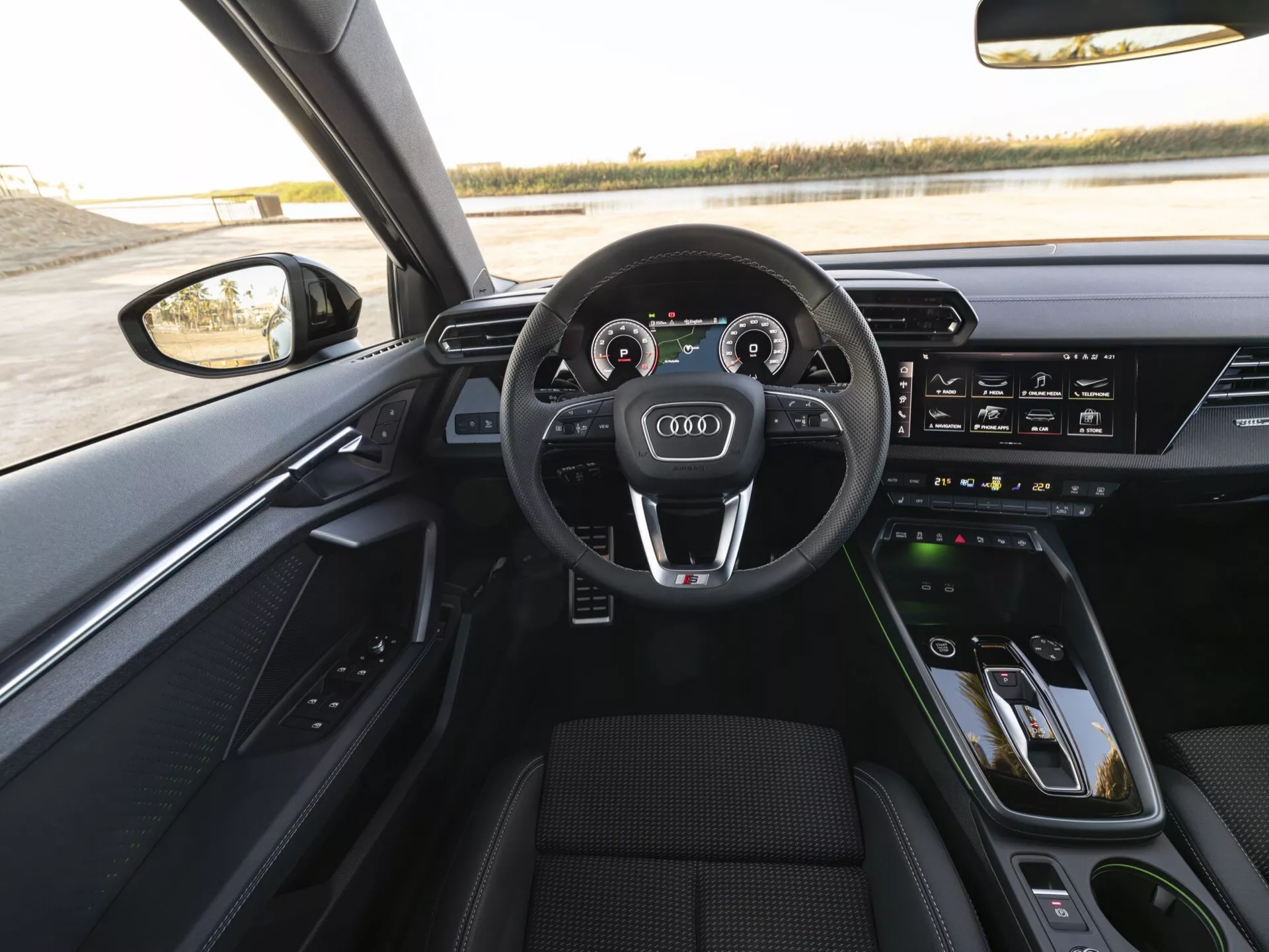 Pogled na notranjost vozila Audi A3 2024 (8Y-Facelift) iz perspektive voznika, ki prikazuje trospeščni volan, oblečen v usnje, z multifunkcijskimi gumbi, digitalni instrumentni sklop, znan kot Audi Virtual Cockpit, MMI dotik zaslon na sredinski konzoli, kontrole klimatske naprave in nadzor premium avdio sistema na voznikovih vratih.