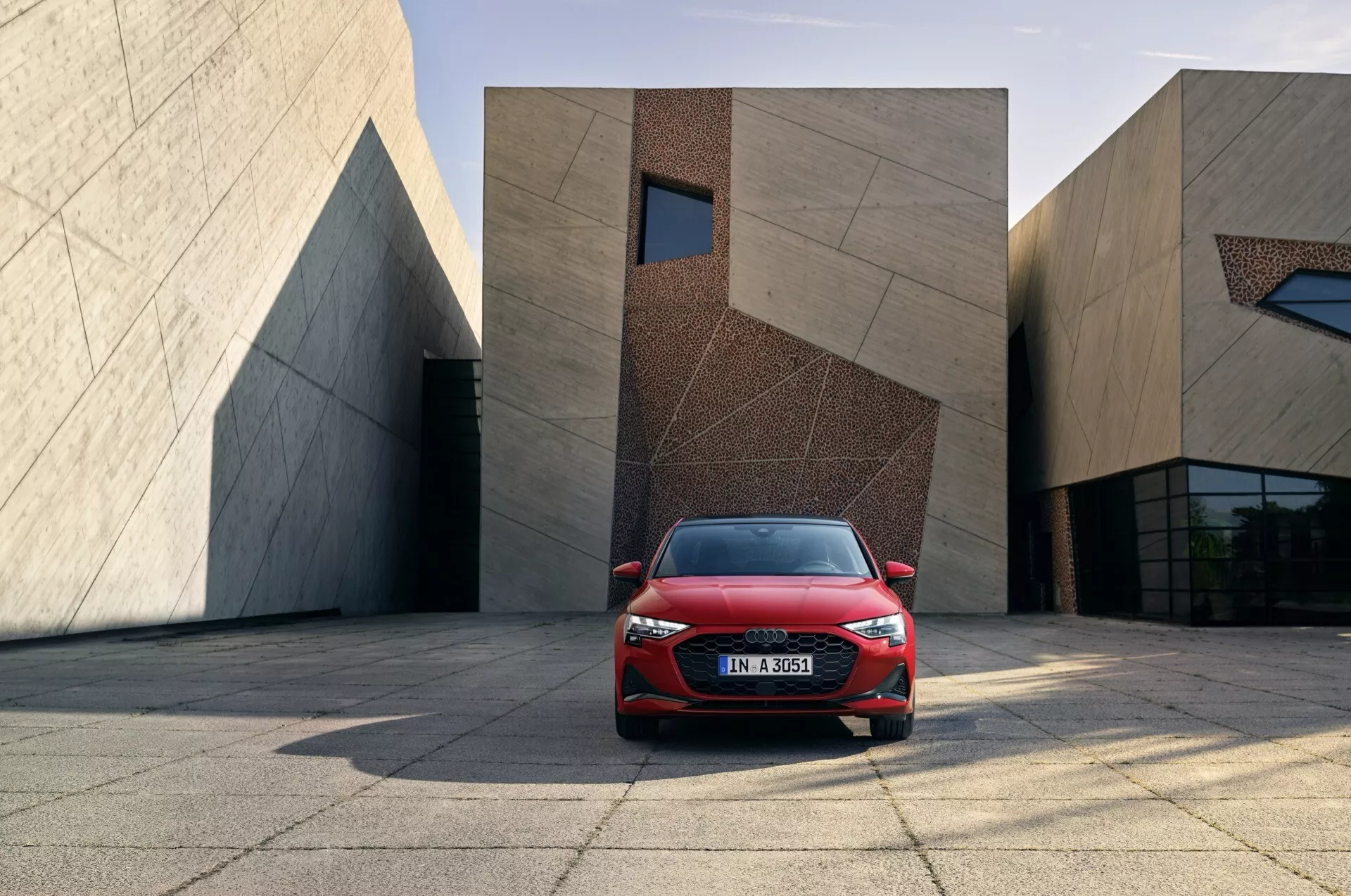 Rdeče Audi A3 (8Y-Facelift) letnik 2024 z modernimi LED žarometi in aerodinamičnim dizajnom, postavljeno na mestnem trgu z modernimi stavbami v ozadju