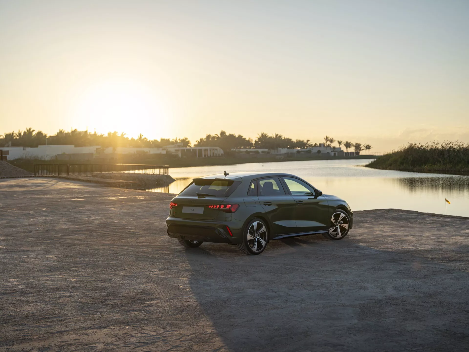 Sedan Audi A3 (8Y-Facelift) letnik 2024, parkiran na prostem ob sončnem vzhodu ali zahodu, z zadnjega tričetrtinskega kota, ki prikazuje stranski profil, kolesa in tehnološke značilnosti v slikovitem okolju