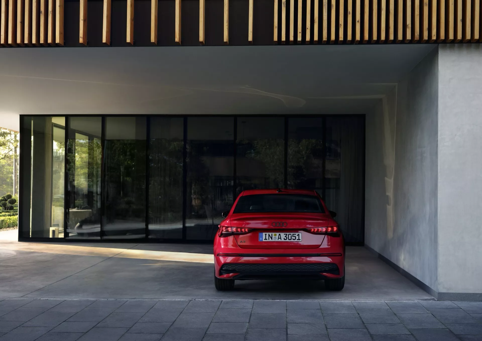 Rdeč Audi A3 (8Y-Facelift) letnik 2024, fotografiran iz zadnjega kota treh četrtin z poudarkom na LED zadnjih lučeh, dvojnem izpušnem sistemu in subtilnem zadnjem spojlerju, parkiran na prostem pred moderno stavbo