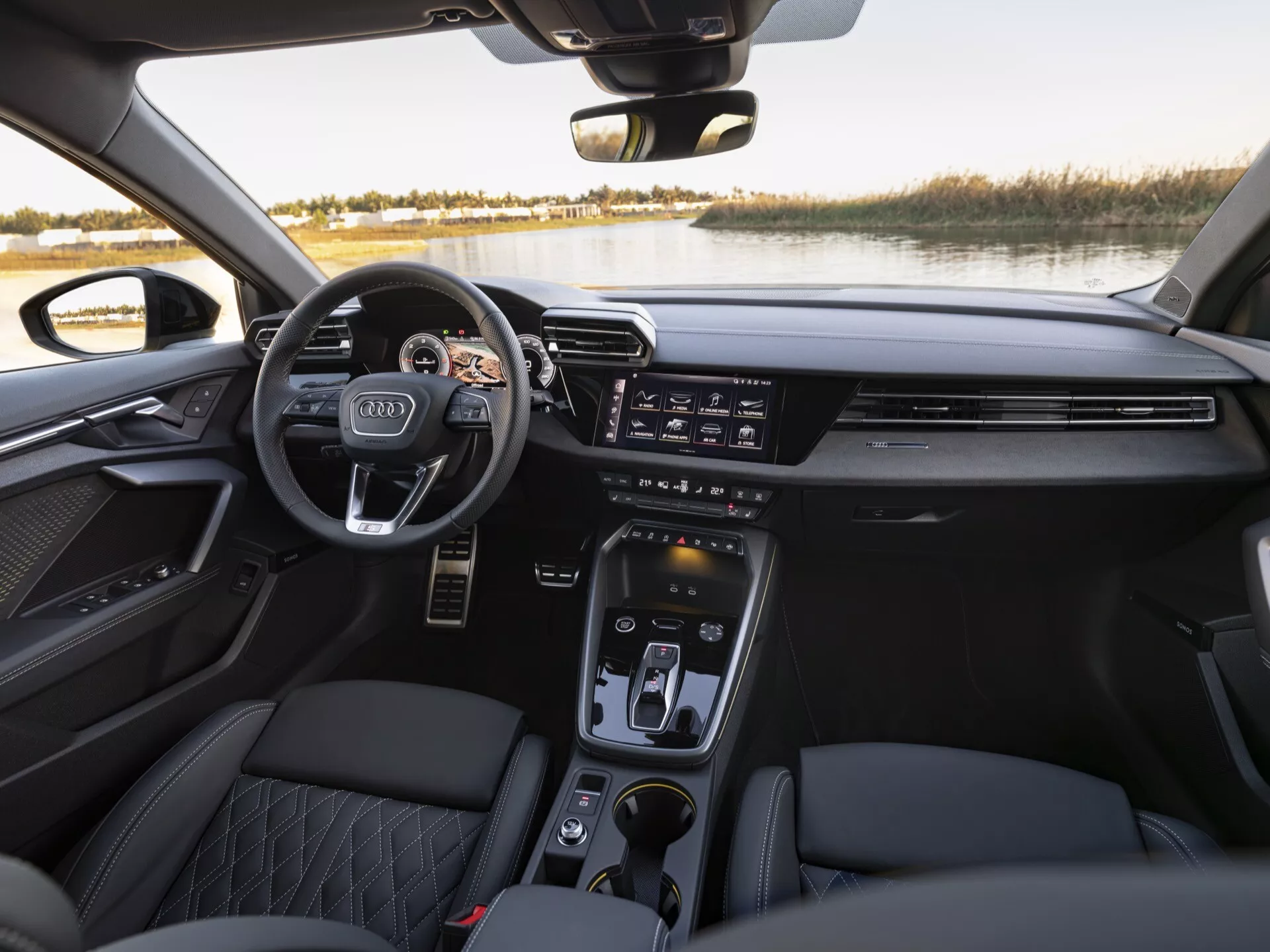 Notranji pogled na Audi A3 2024 (8Y-Facelift), ki prikazuje volan z nameščenimi kontrolami, elegantno armaturo z horizontalnimi zračniki, širok zaslon na dotik za informacijsko-zabavni sistem, gumbe za nadzor klime, elektronski izbirnik prestav, sedeže iz prešitega usnja in vrata panela s premium zvočnim sistemom