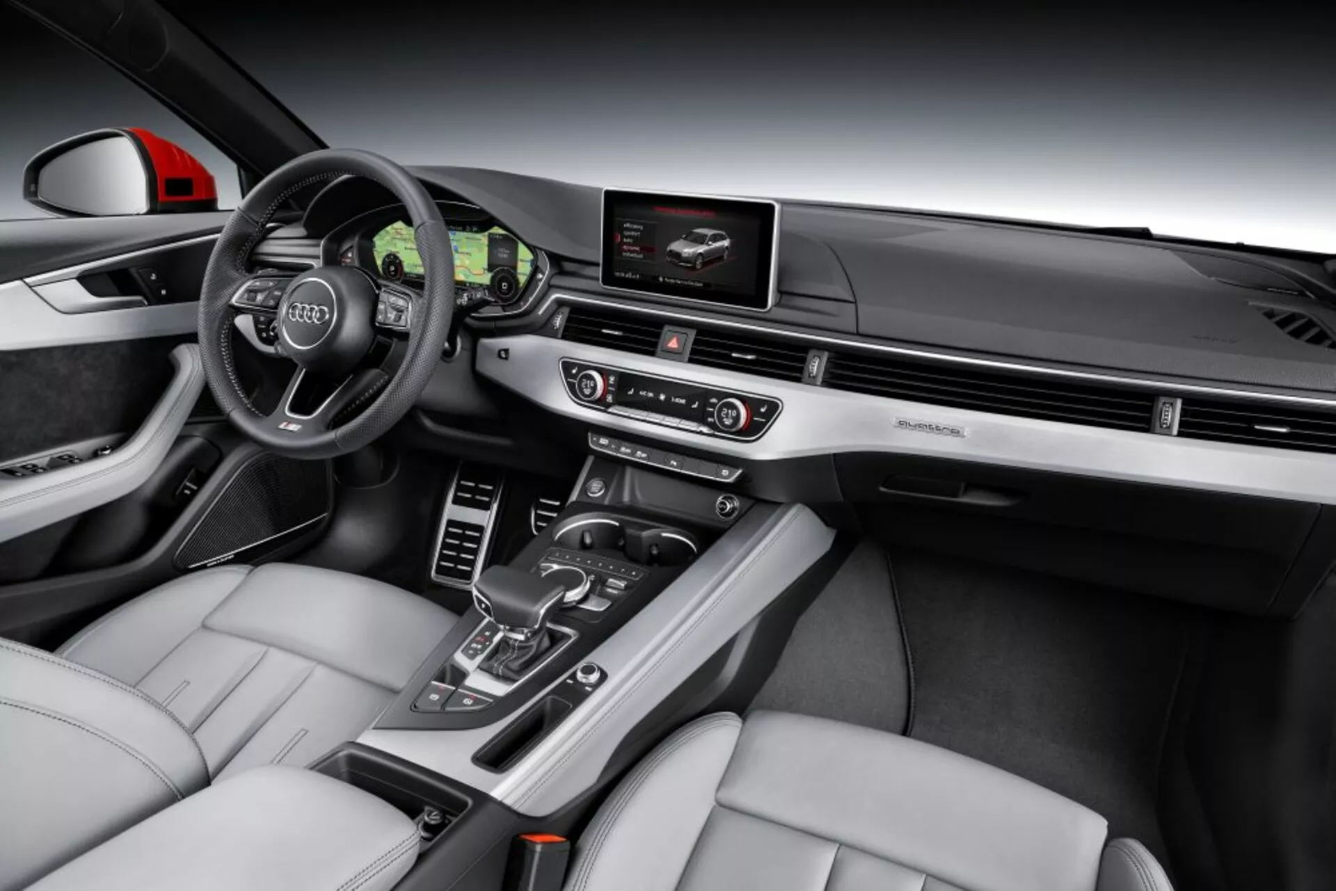 Pogled na notranjost Audi A4 Limuzine 2019 z osredotočenjem na voznikovo stran z volanom s tremi kraki, delni pogled na instrumentno ploščo, navigacijo na zaslonu za zabavo in informacije, avtomatsko prestavno ročico, svetlo usnjene sedeže z izrazitimi bočnimi ojačitvami ter luksuznimi lesenimi in krtačenimi kovinskimi detajli