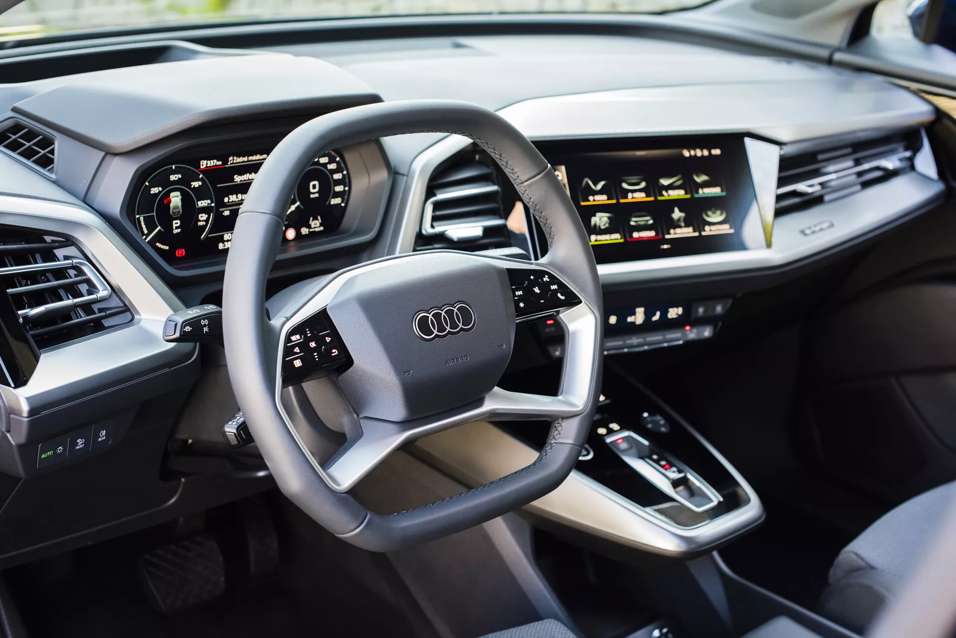 Notranjost Audi Q4 e-tron 2021 z vidika voznikove strani, predstavlja multifunkcijski volan z logotipom Audi, digitalno instrumentno ploščo, sredinsko konzolo z ročico menjalnika, na dotik občutljive kontrole HVAC, zaslon infotainment sistema, elegantno armaturno ploščo z integriranimi zračniki in luksuzno oblazinjena vrata iz usnja, prikazujejoč sodobno tehnologijo avtomobilov in lastnosti luksuznih vozil.