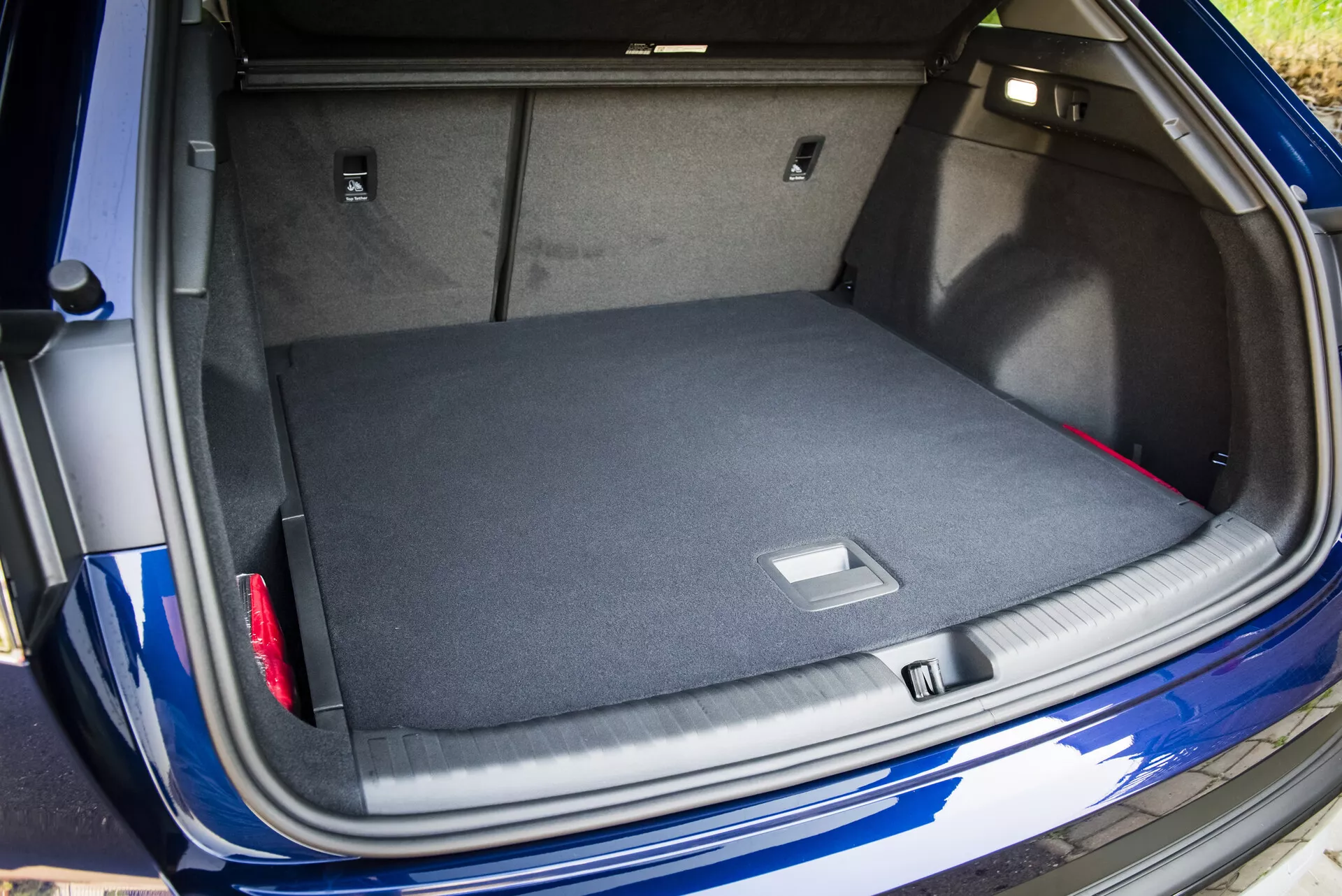 Pogled na prostoren, s preprogo obložen prtljažnik Audija Q4 e-tron 2021 z odprtim pokrovom prtljažnika, ki prikazuje pametne rešitve za shranjevanje in pogled na njegov kovinsko modri zunanji del z vidnim parkirnim senzorjem