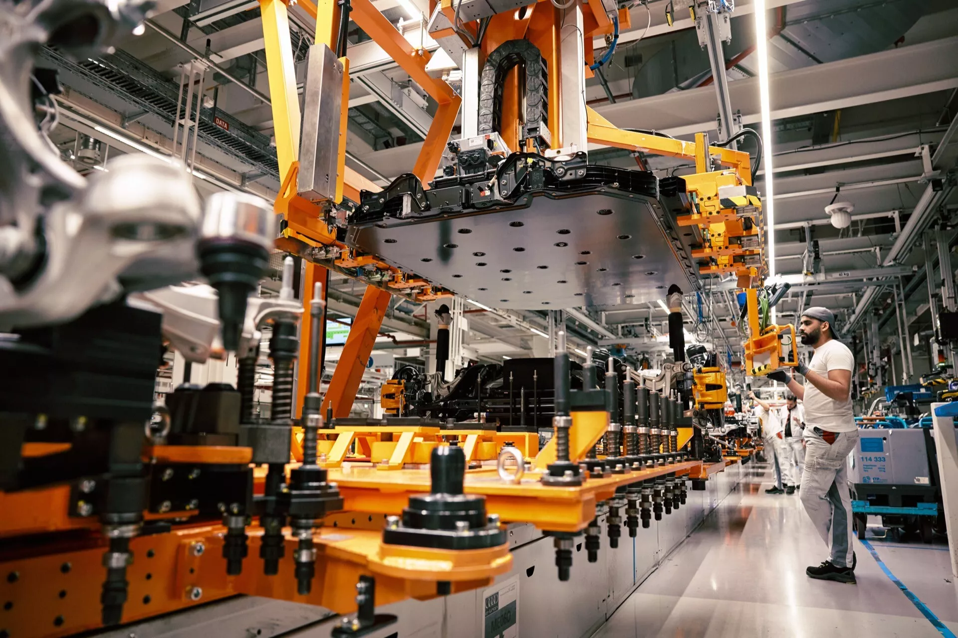 Sestavljanje Audi Q8 e-tron 2023 v industrijskem obratu, prikazovanje robotske roke, ki manipulira s podvozjem vozila brez vrat ali koles na avtomobilski montažni liniji