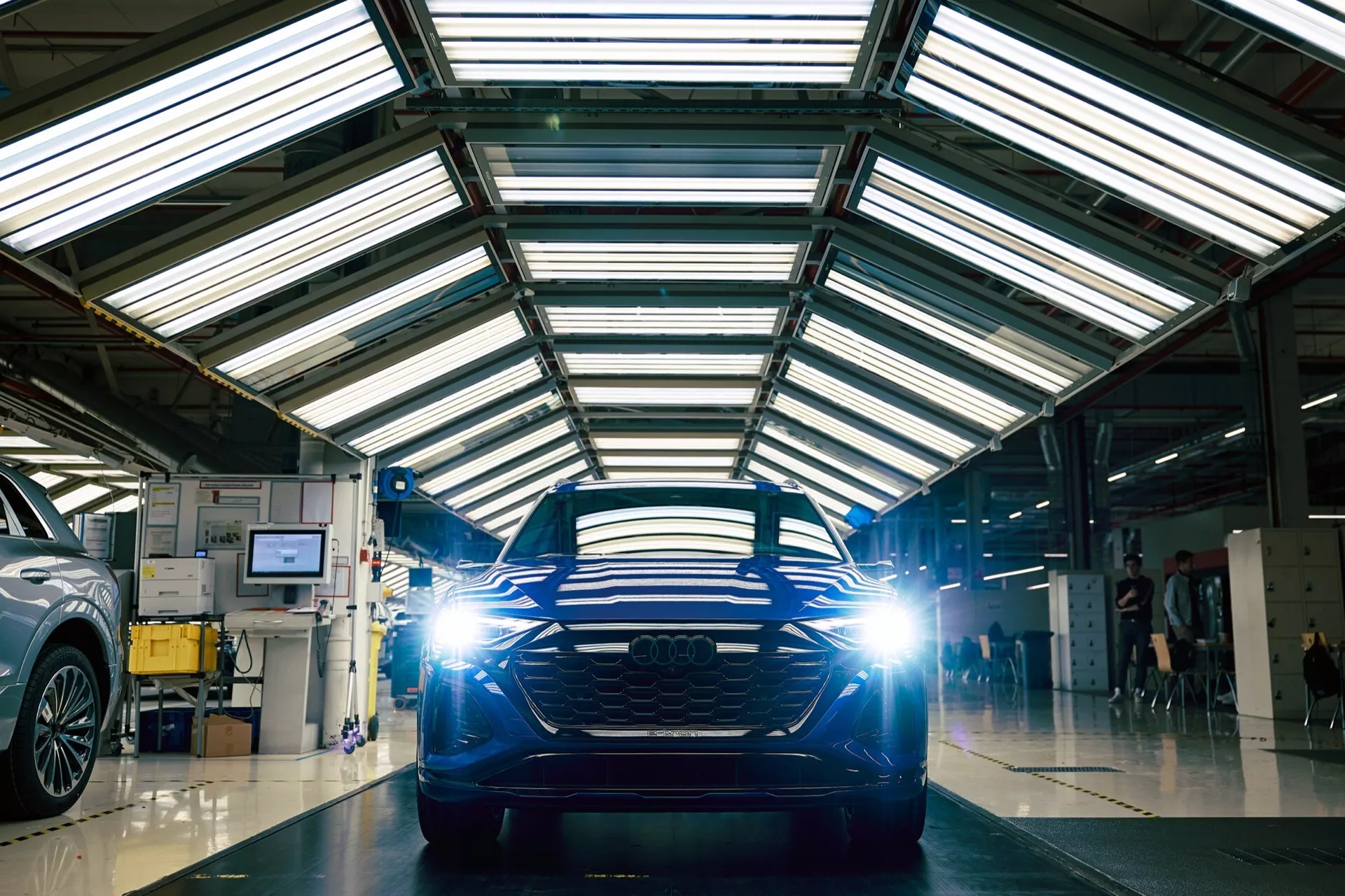 Sprednji pogled na Audi Q8 e-tron 2023 v delavnici z odsevnim tlom, poudarjajoč njegovo horizontalno rešetko in LED žaromete.