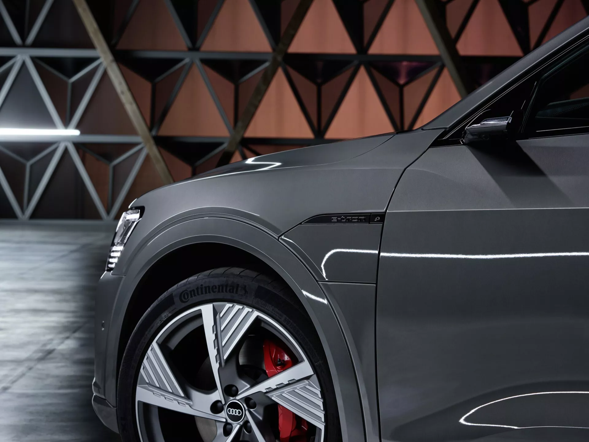 Podroben stranski pogled na Audi Q8 e-tron 2023 s poudarkom na sprednjem četrtinskem panelu, prikazuje večkrako zlitinsko kolo, visokozmogljivo pnevmatiko Continental, rdečo zavoro z velikim diskom in sijajnim lakom s športnimi oblikovnimi linijami